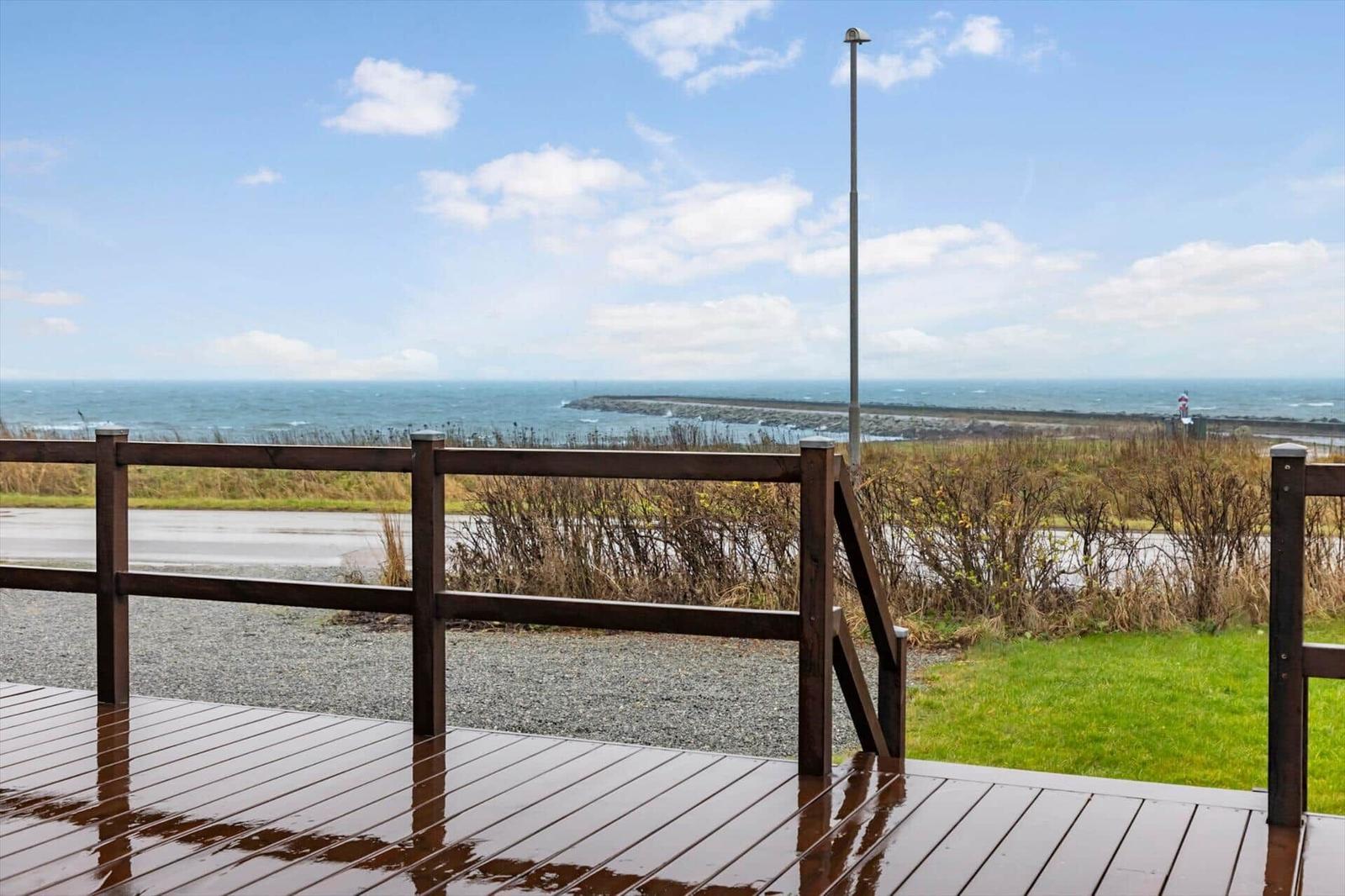 Wooden terrace with view of the sea and a lighthouse in the distance.