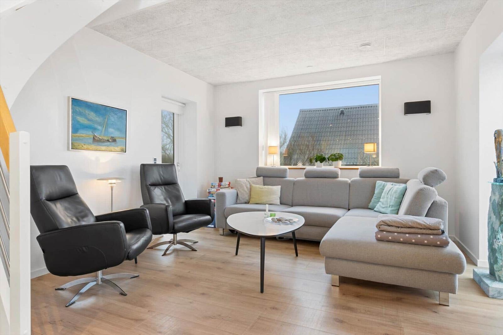 Living room with gray sofa, two black chairs, and wooden floor. Large windows and wall art.