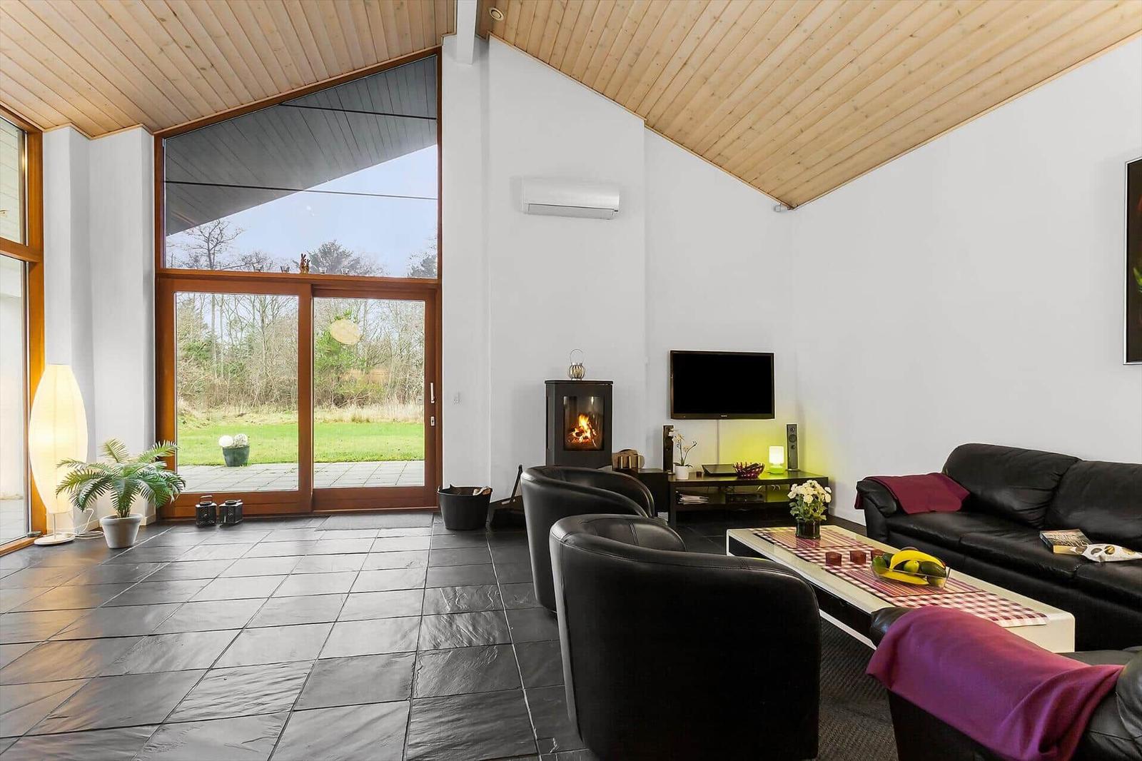 Living room with fireplace, TV, and black leather furniture. Large glass door to garden.