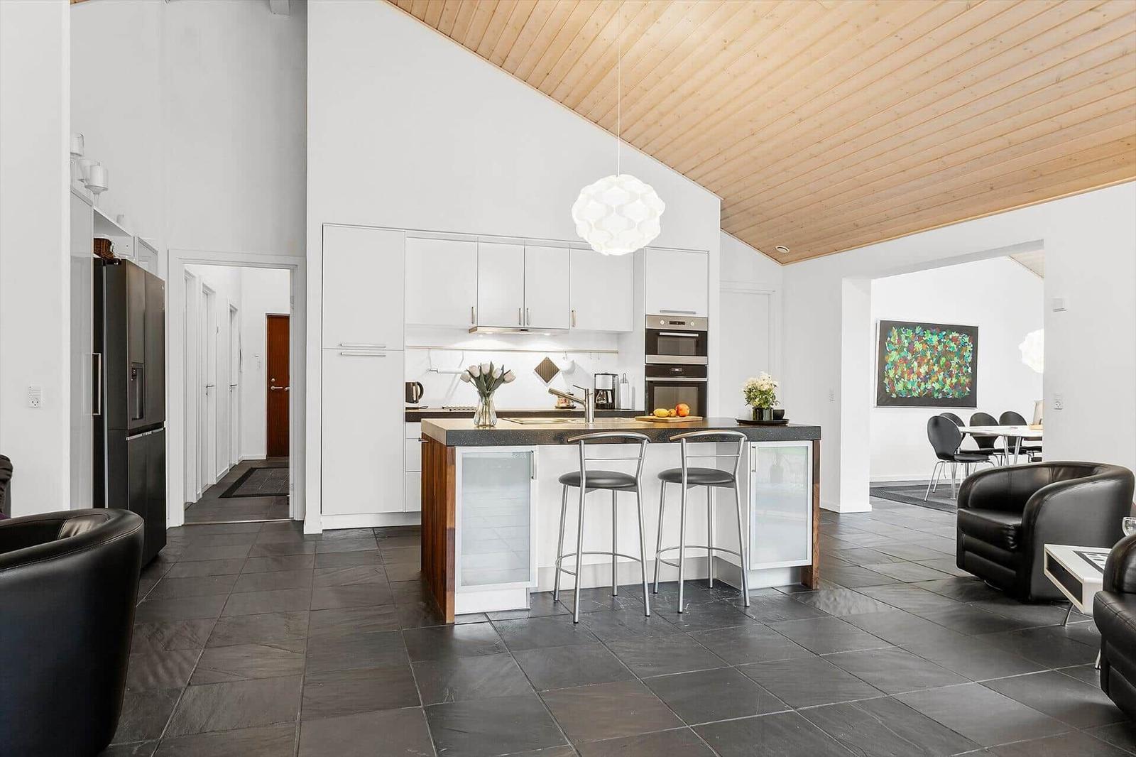 Kitchen with island, black tiles, and wooden ceiling. Dining and living area in background.