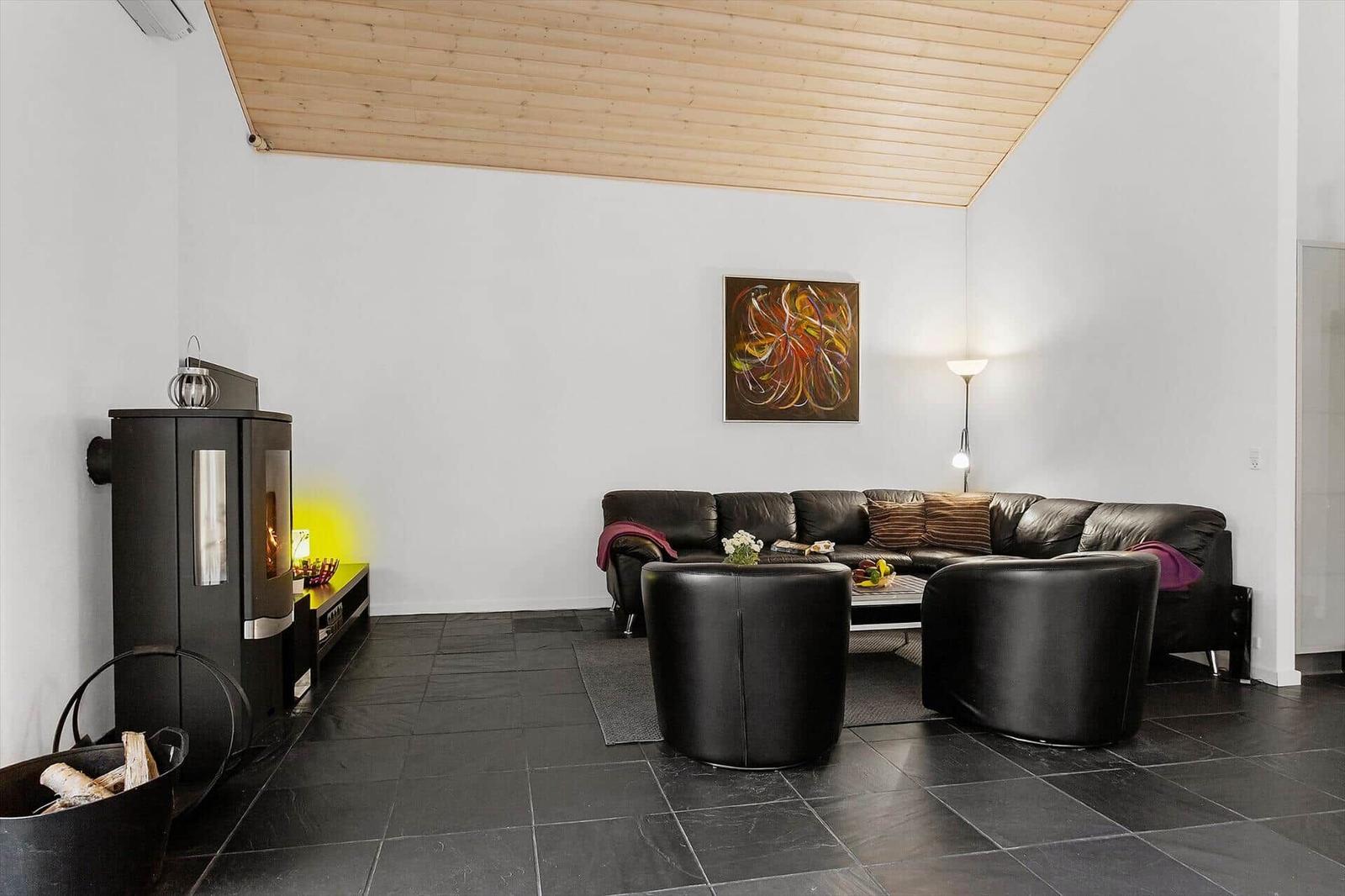 Living room with wooden ceiling, sofa, chairs, and wood stove.