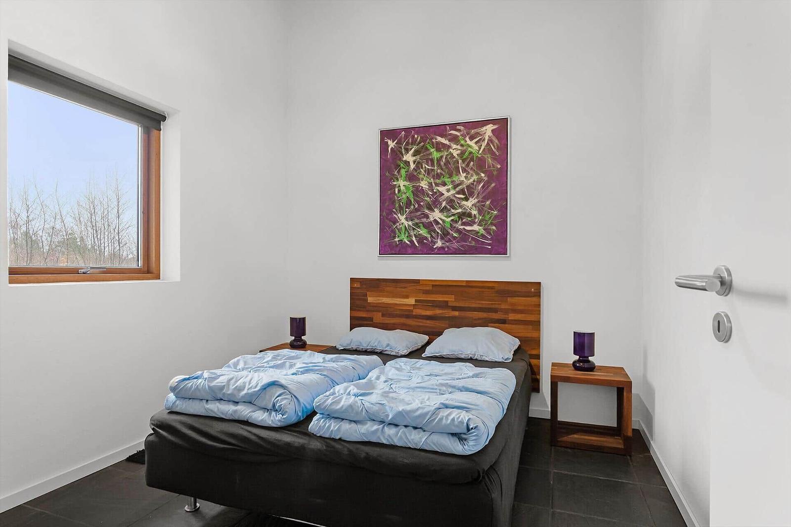 Bedroom with bed, nightstands, and wall art. Window shows exterior view.