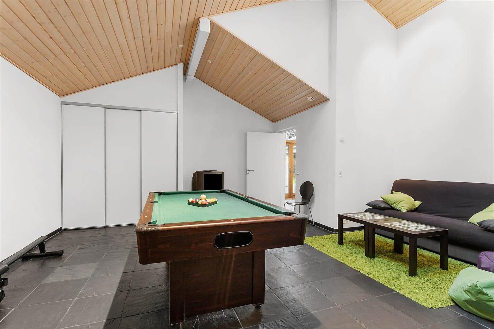 Room with pool table, sofa, and green rug. Wooden ceiling and white walls.