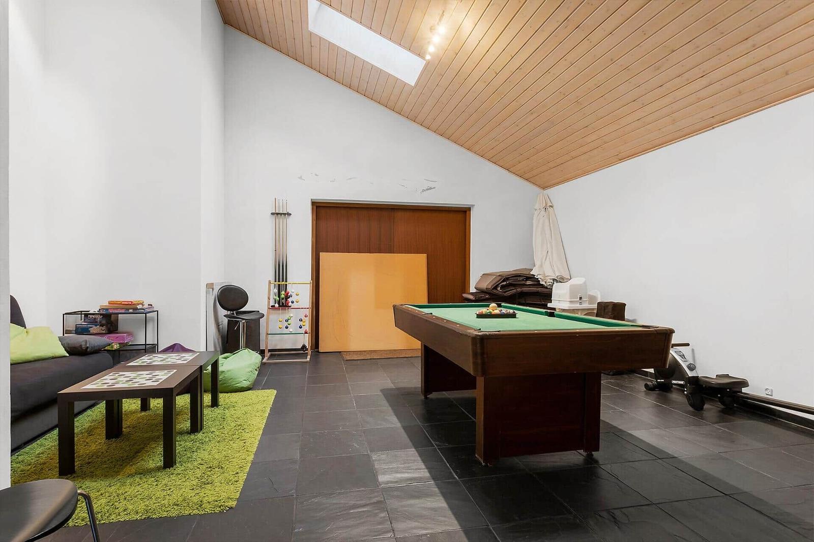 Room with pool table, sofa, table, and green rug. Wooden ceiling and black tiles.