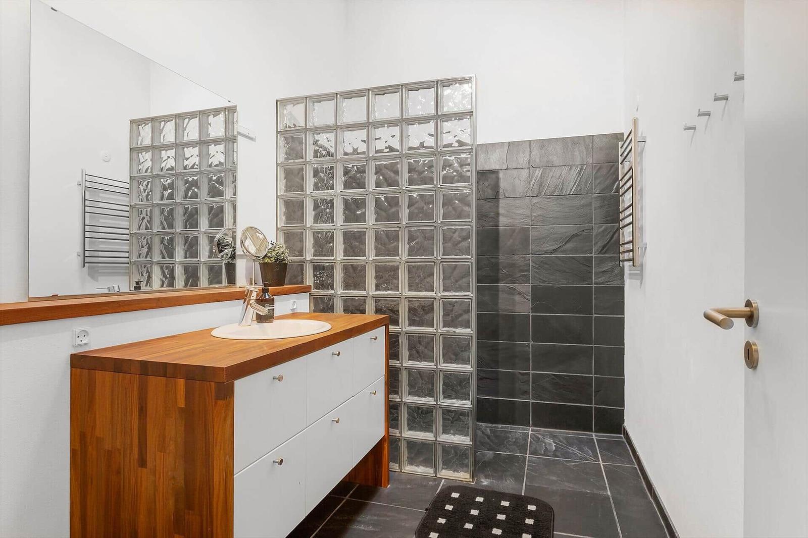 Bathroom with sink, shower, and mirror. Glass blocks and dark tiles.