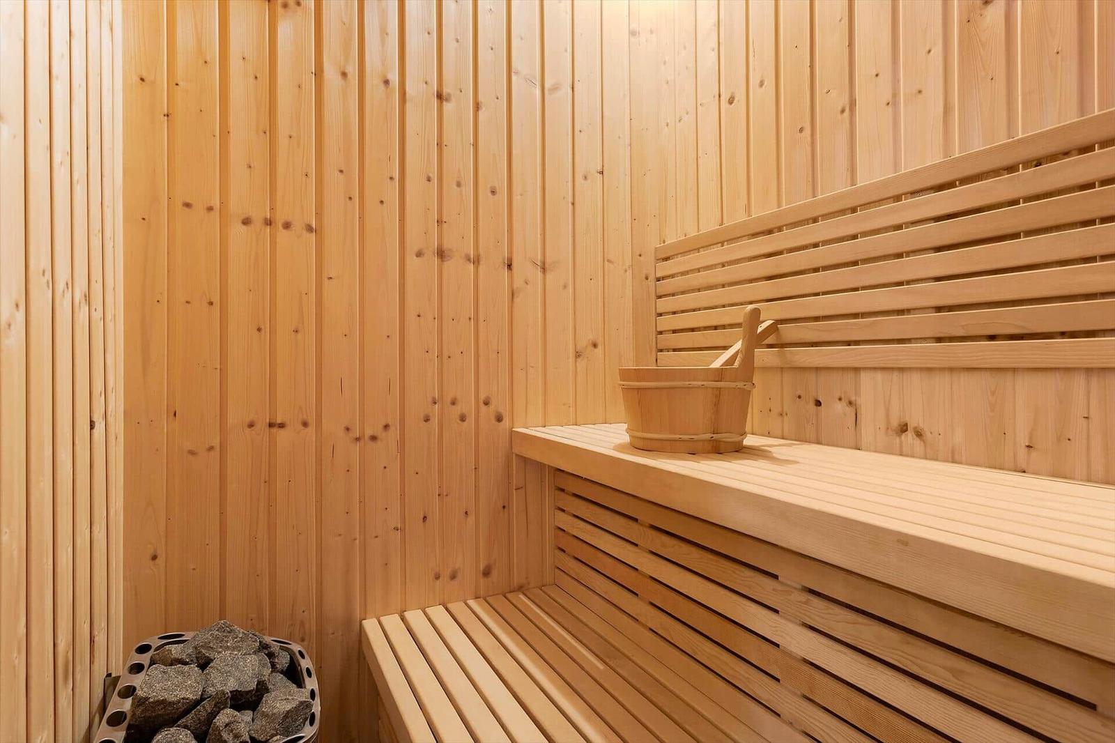 Sauna with wooden bench and bucket. Stones in stove. Wooden walls.