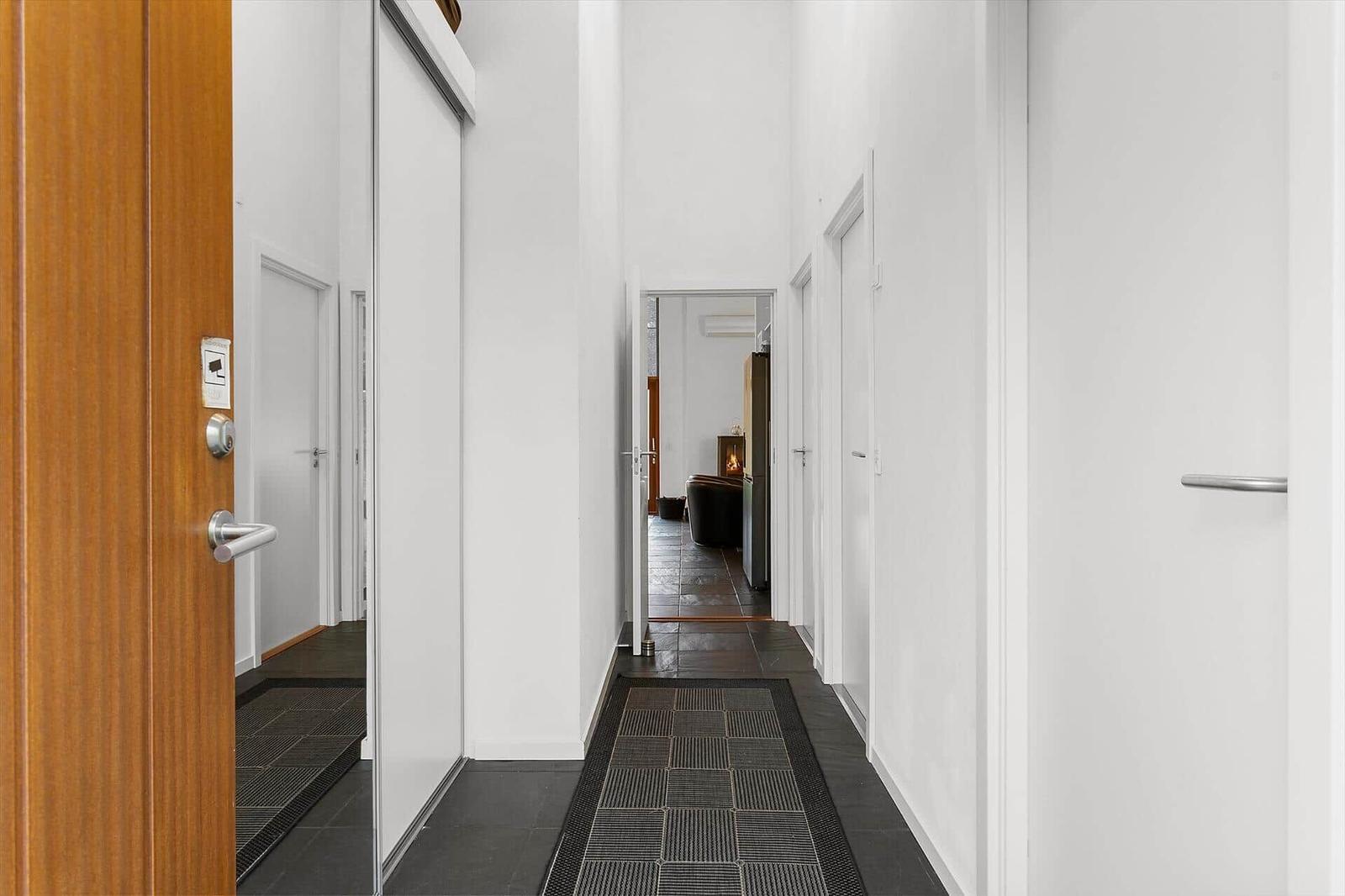 Hallway with white walls, dark floor, and door to living room with fireplace.