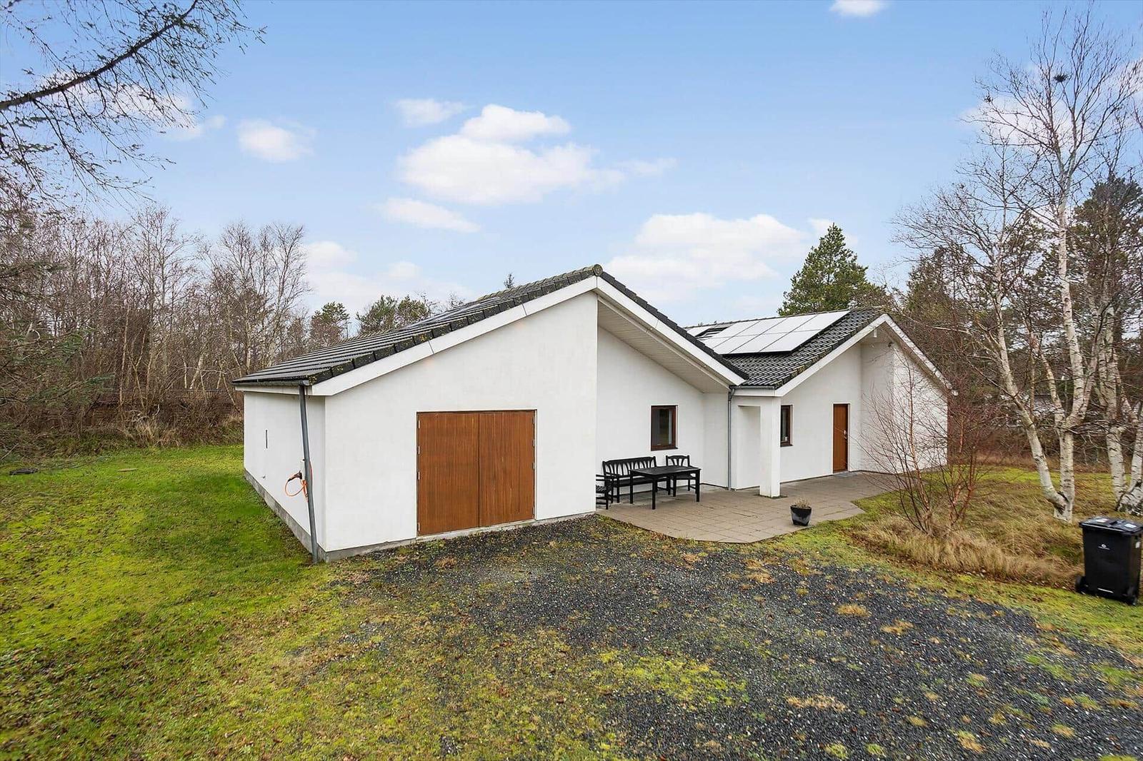 Modern white villa with terrace, garden, and solar panels. Surrounded by trees.