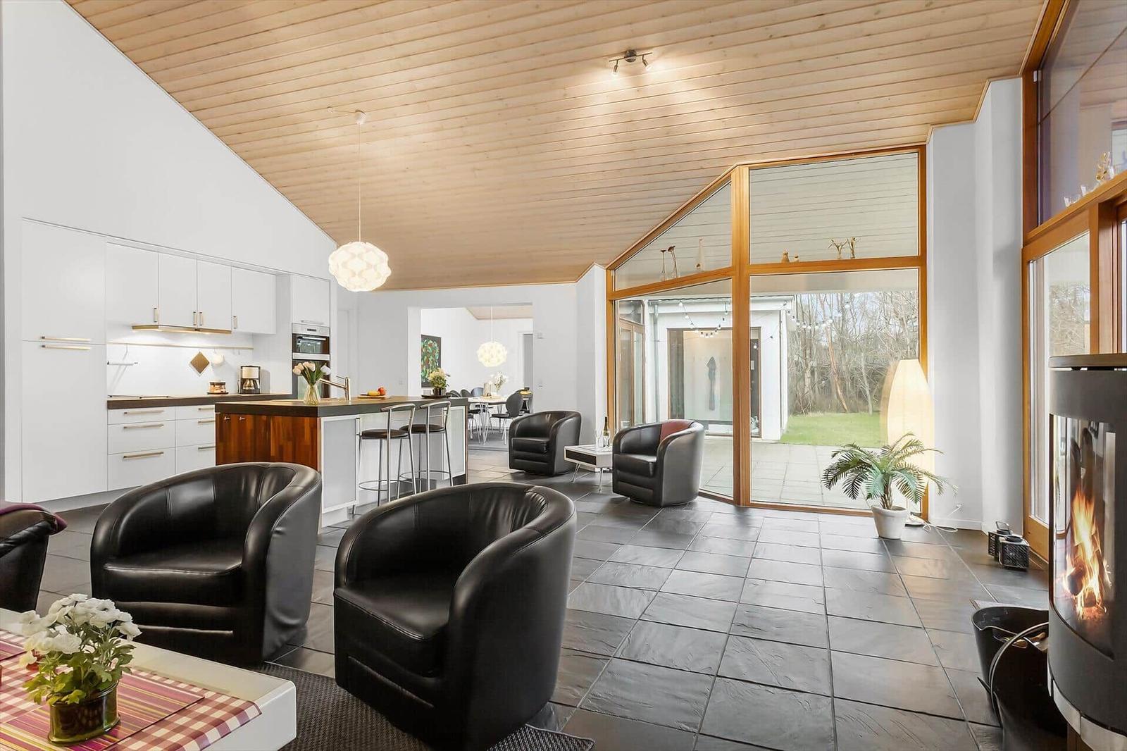 Modern open kitchen and living area with fireplace, black chairs, and wood ceiling.