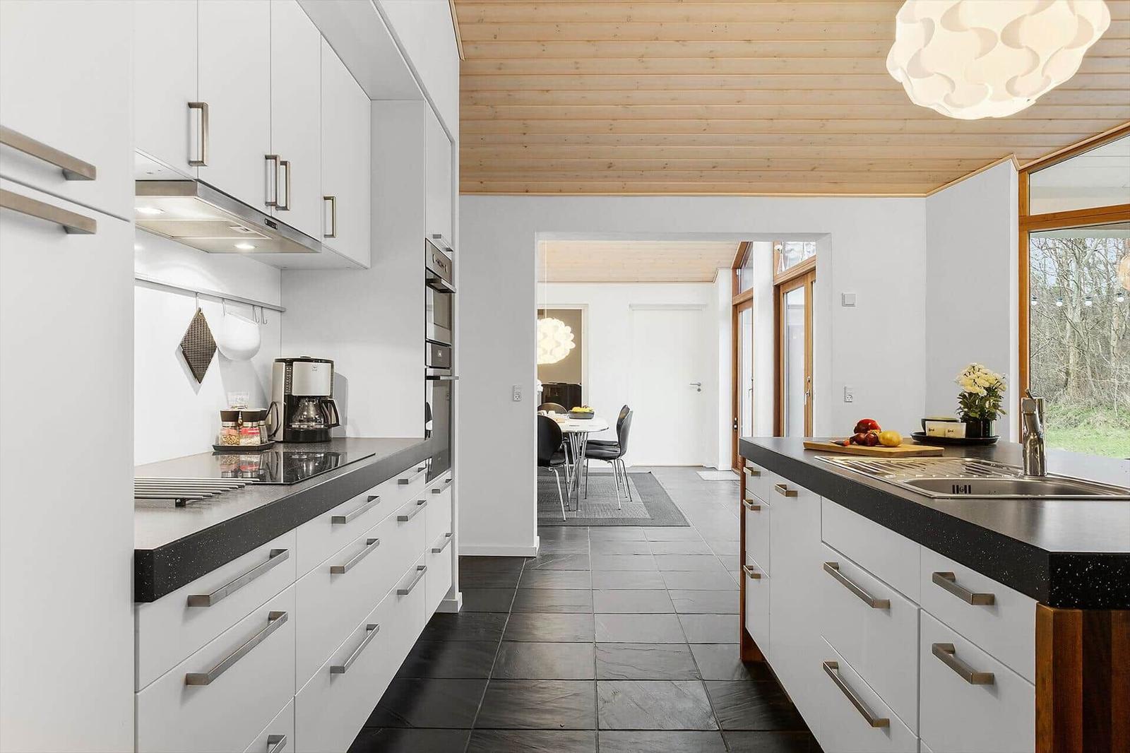 Kitchen with white cabinets, black countertops, and wooden ceiling. View into dining area with table and chairs.