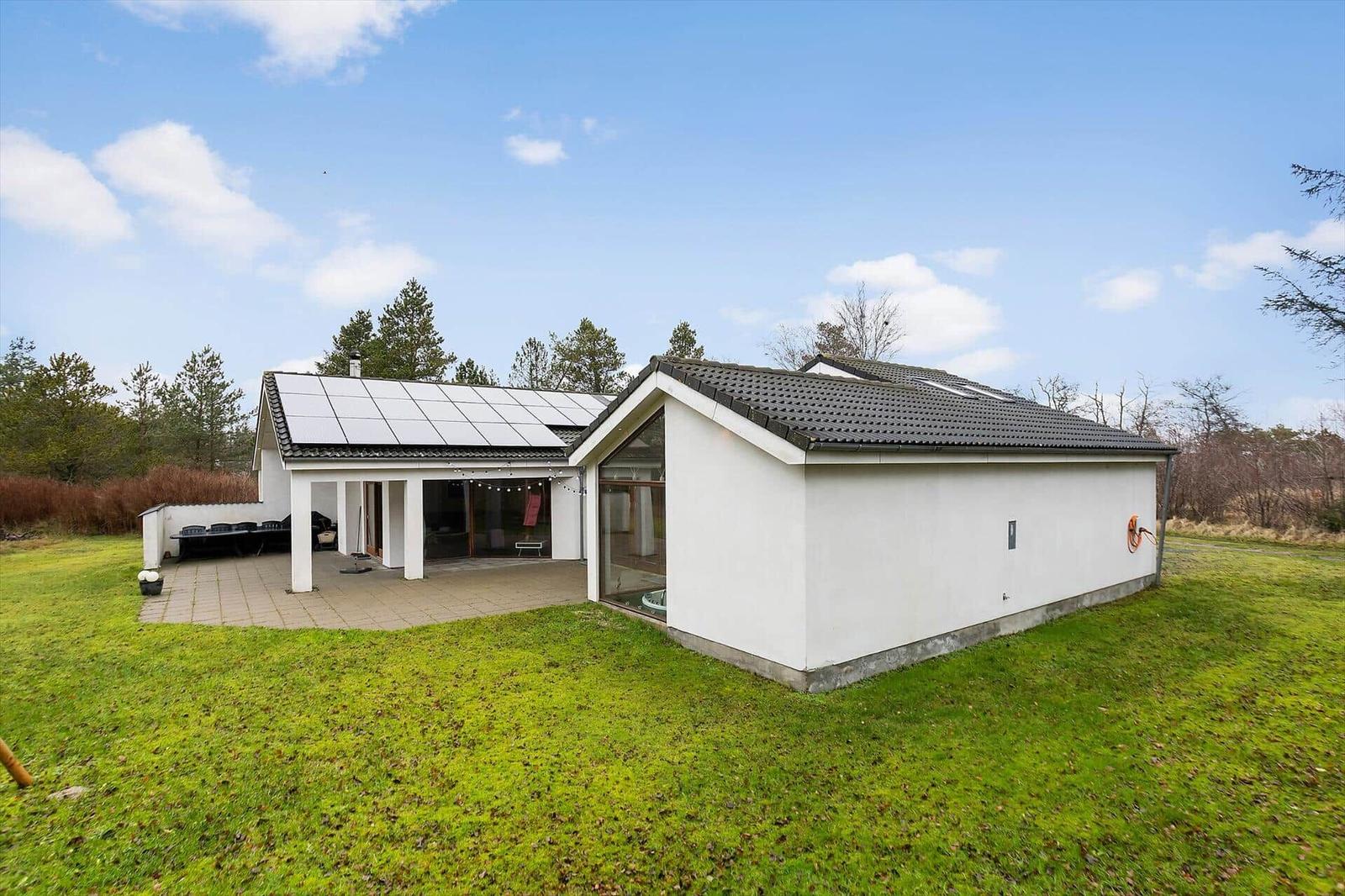Modern villa with solar panels, terrace, and garden. Surrounded by trees and grass.