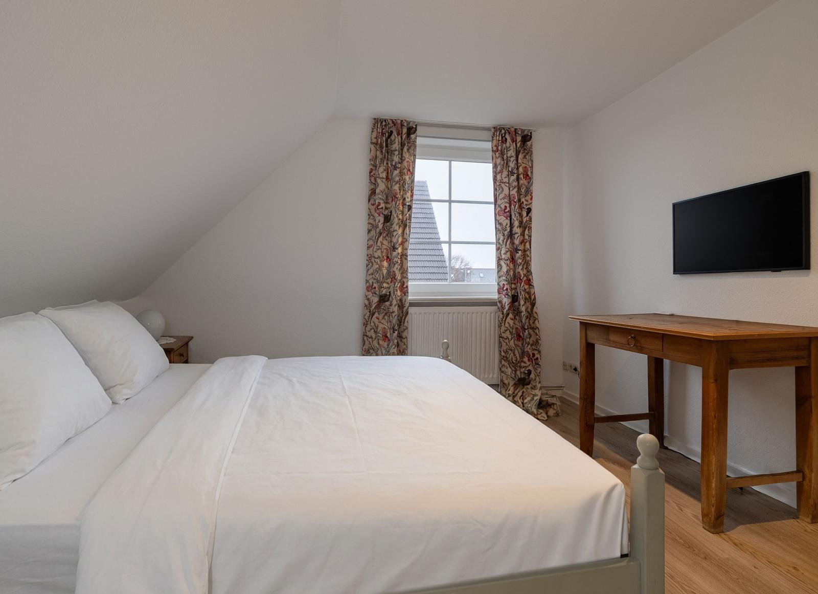 Schlafzimmer mit Dachschrägen, Bett, Schreibtisch und TV.