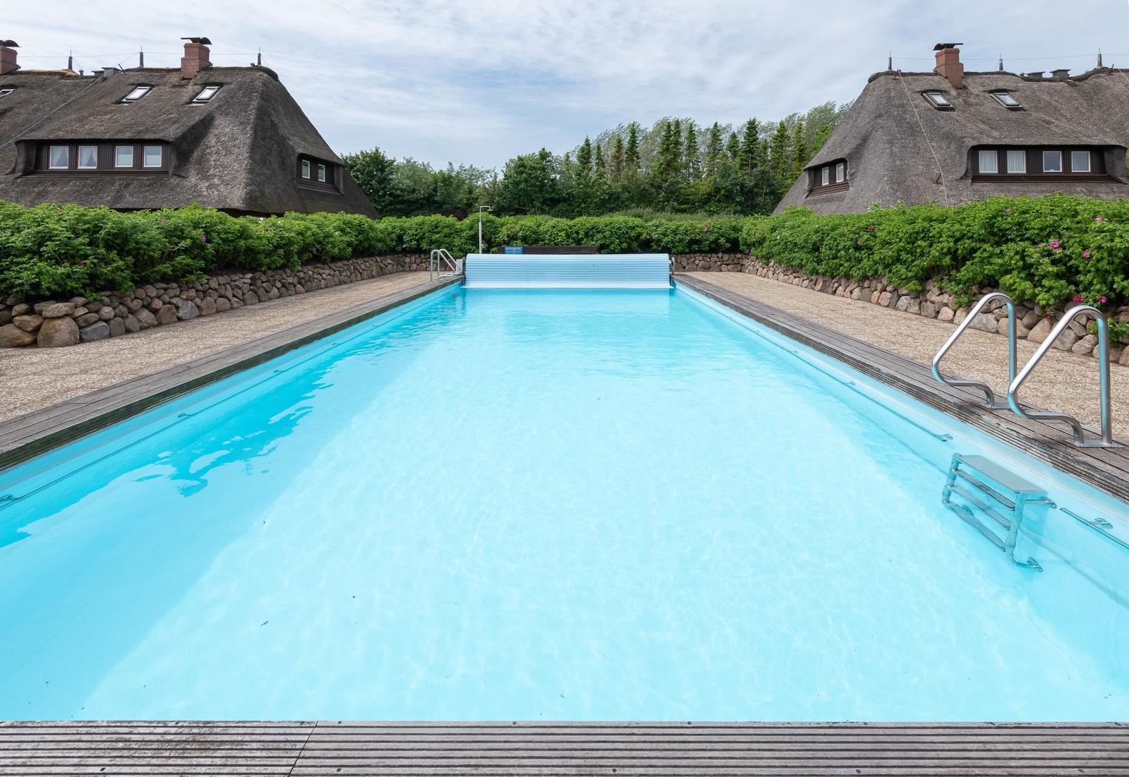 Pool mit Holzumrandung und Dachhäuser im Hintergrund.