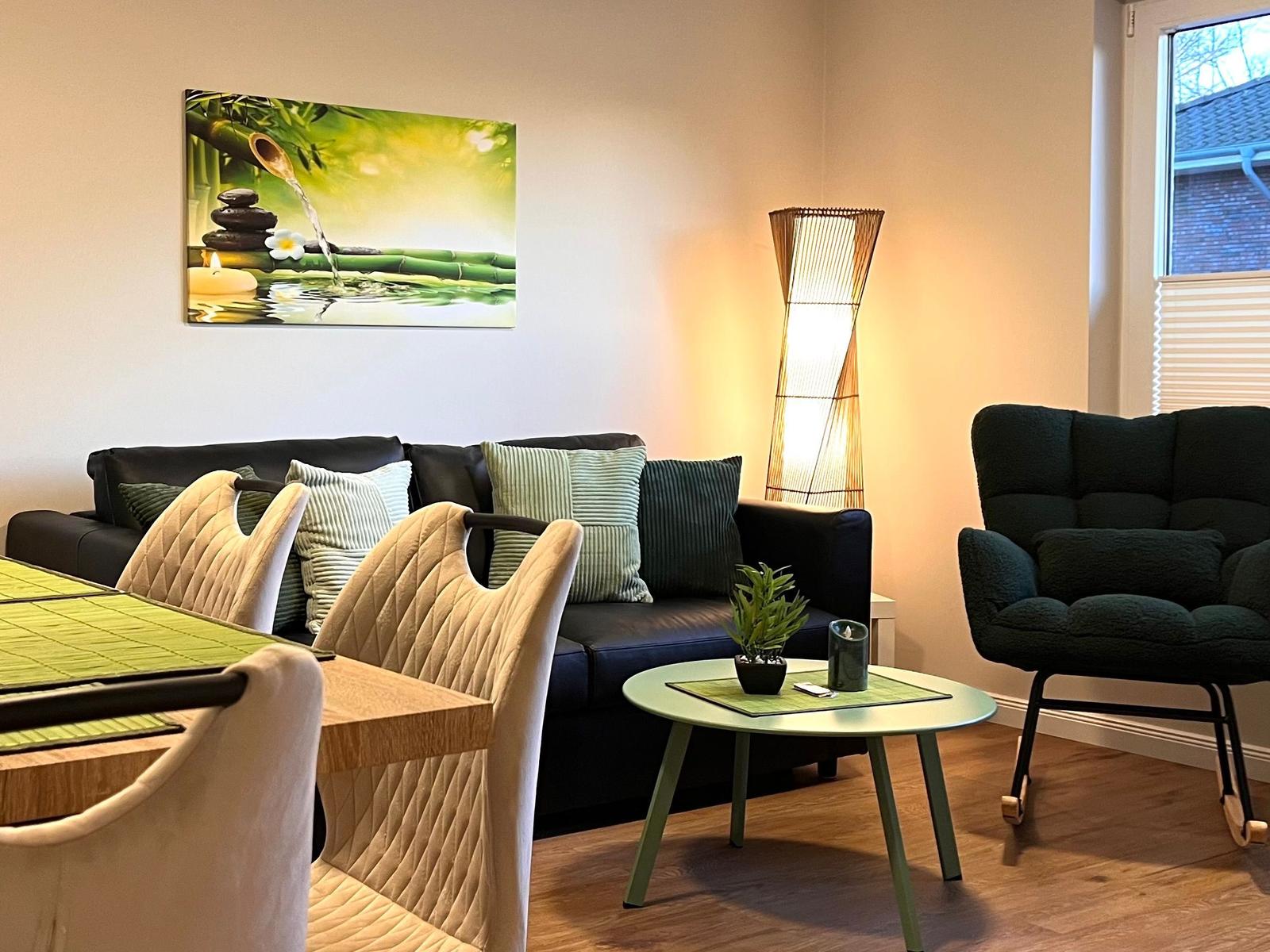 Wohn- und Essbereich mit Sofa, Stuhl und Tisch. Wandbild und Stehlampe sichtbar.