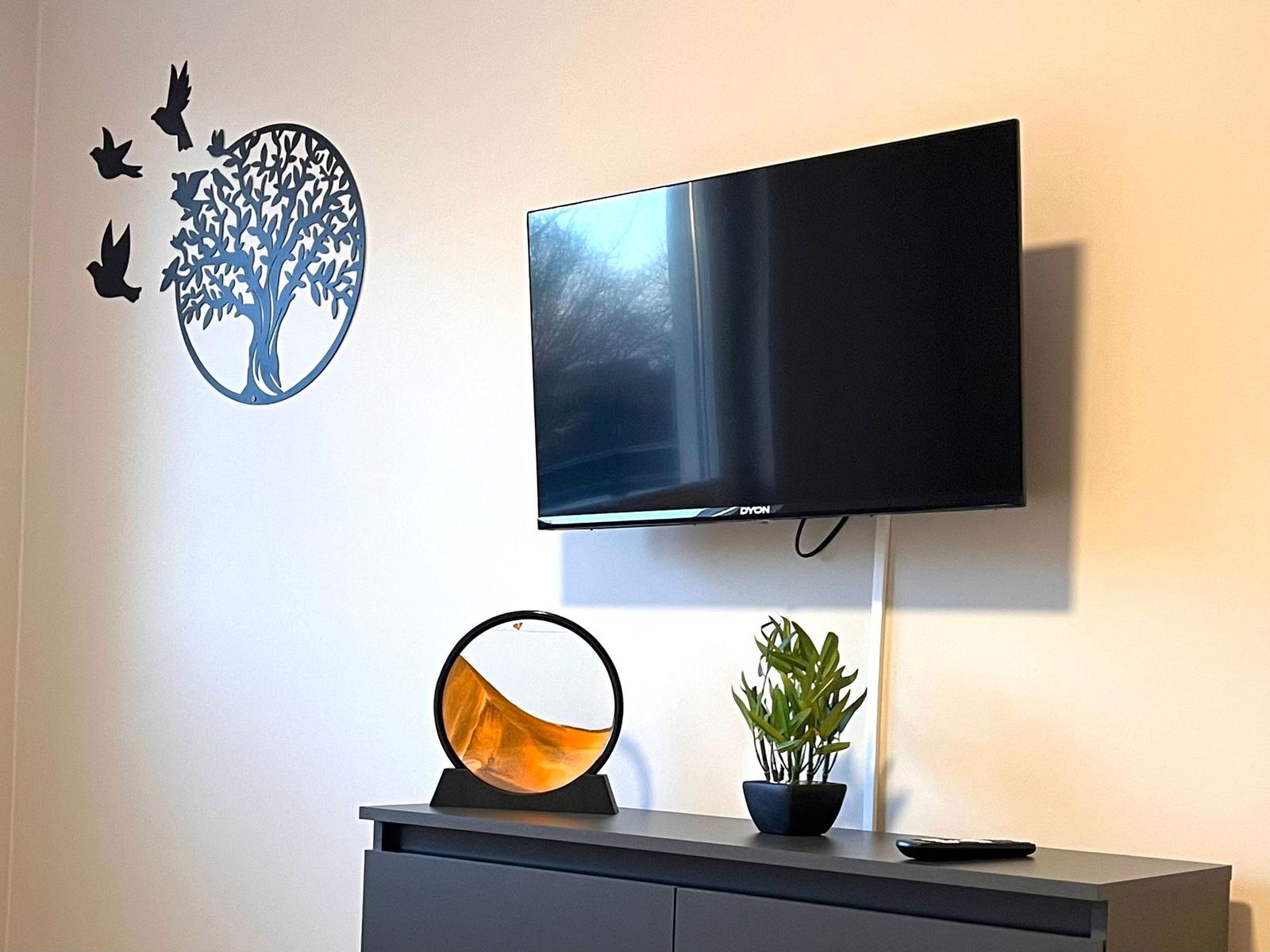 Wandmontierte TV, dekoratives Wandbild und Pflanze auf Konsole