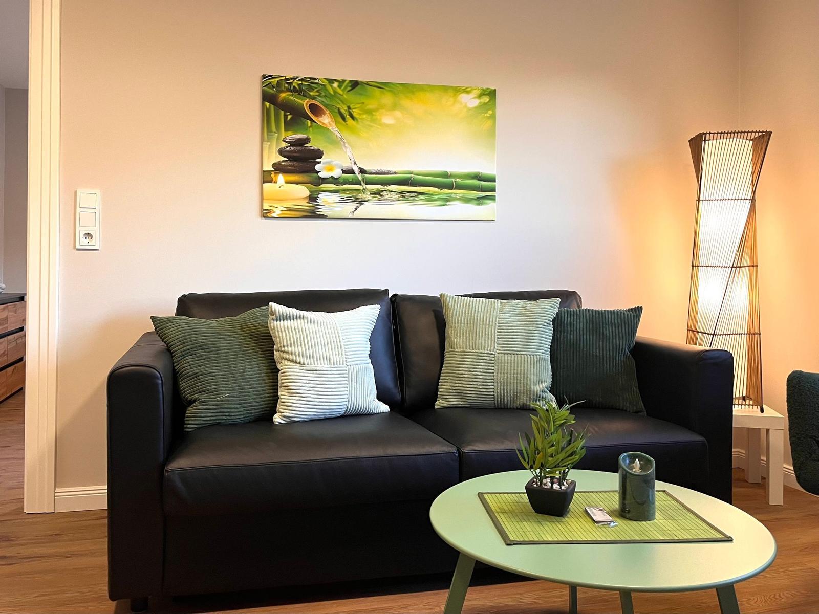 Ein Wohnzimmer mit einem schwarzen Sofa, Kissen und einer Wanddekoration.