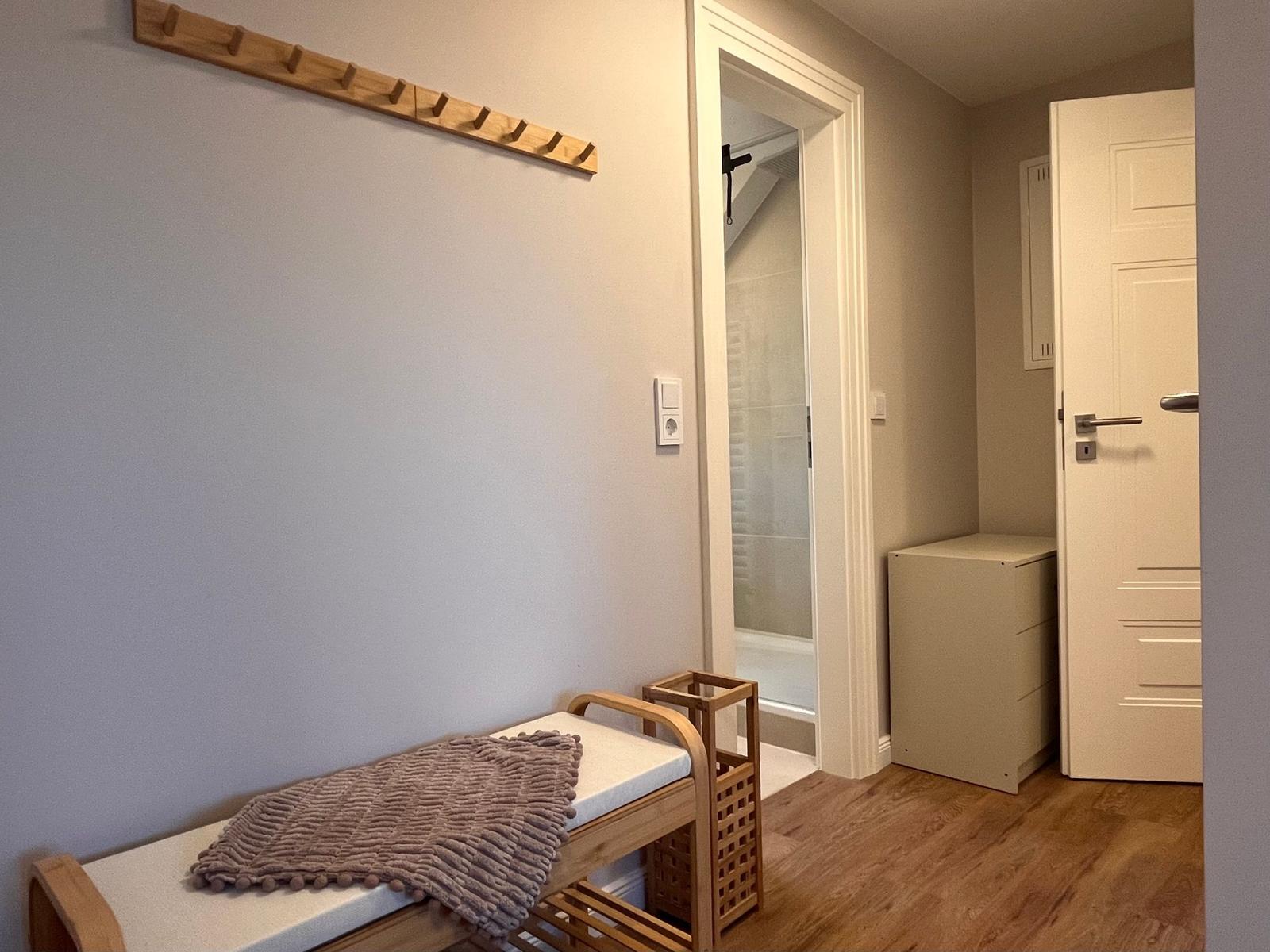 Eingangsbereich mit Holzbank, Hakenwand und Blick in Bad und Schlafzimmer.