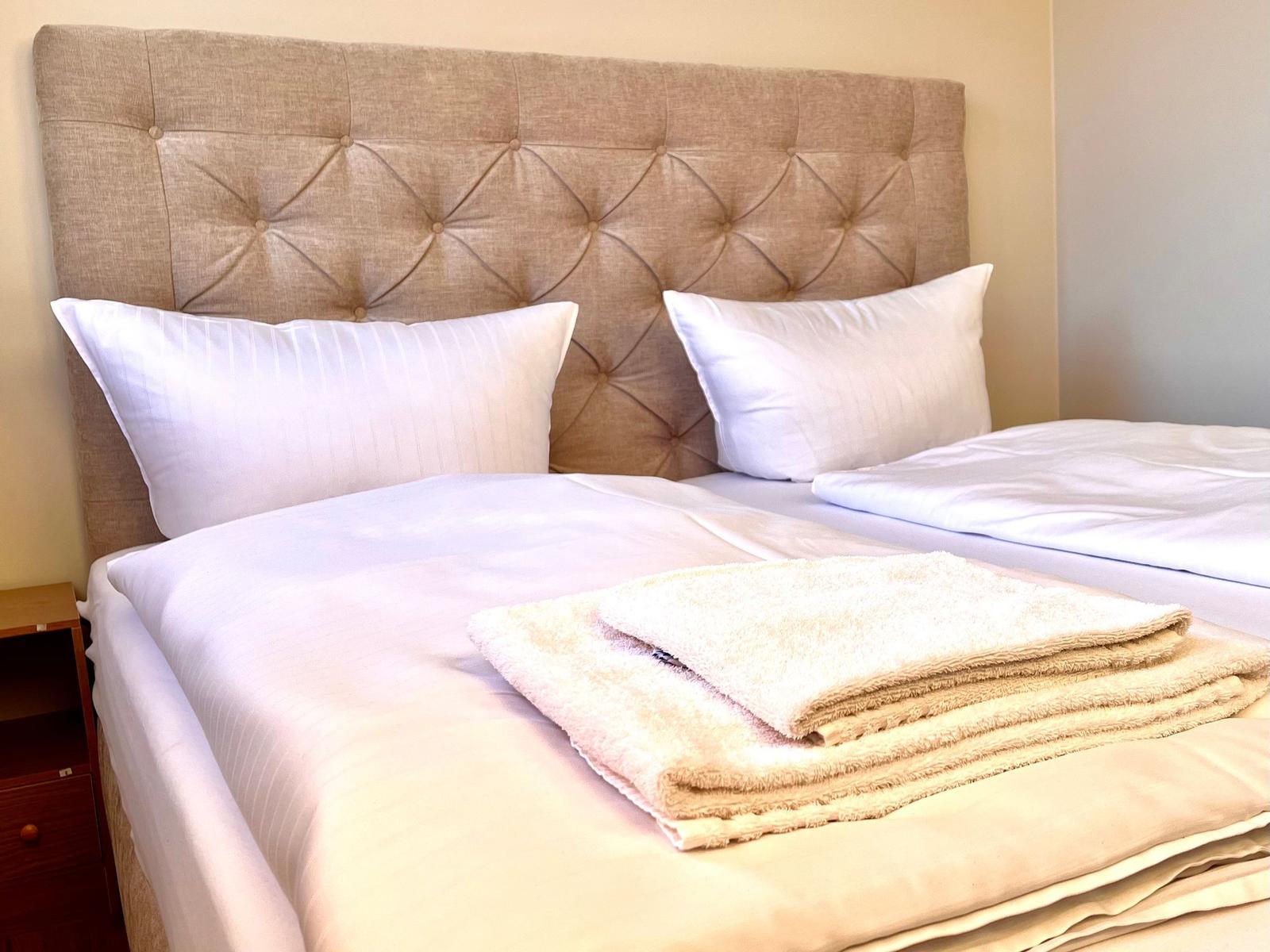 Ein Bett mit weißer Bettwäsche und zwei Kissen. Auf dem Bett liegen gefaltete Handtücher.