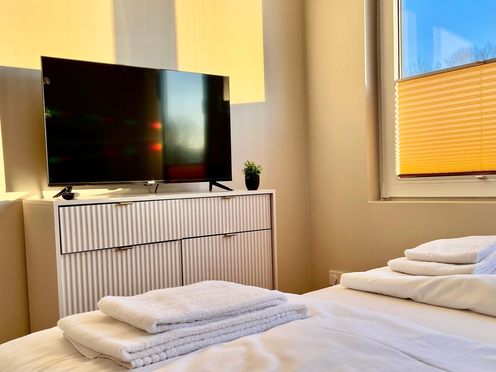 Schlafzimmer mit Bett, Fernseher und Fenster mit Jalousie.