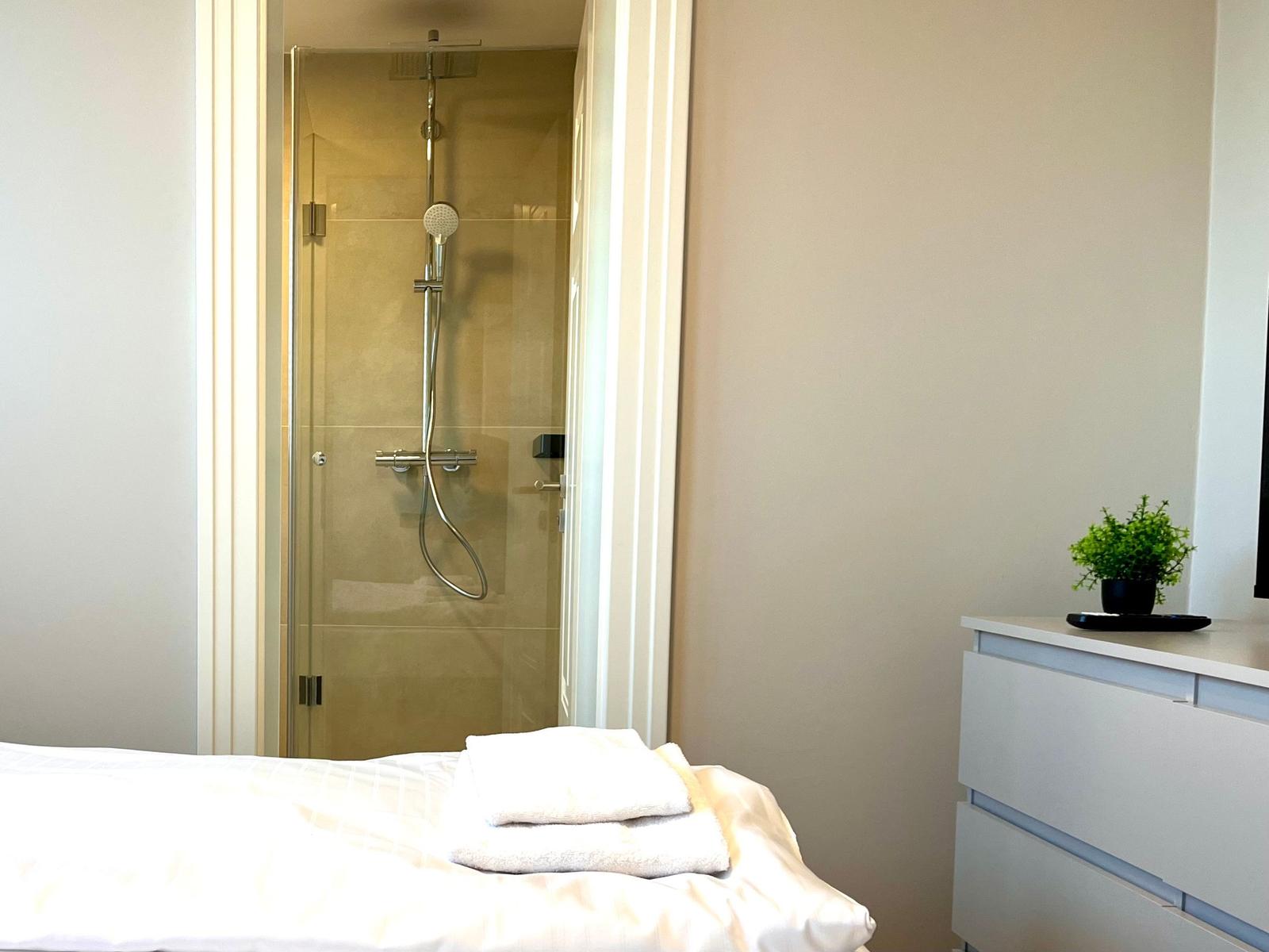 Schlafzimmer mit Dusche und Schrank. Handtuch auf Bett. Pflanze auf Schrank.