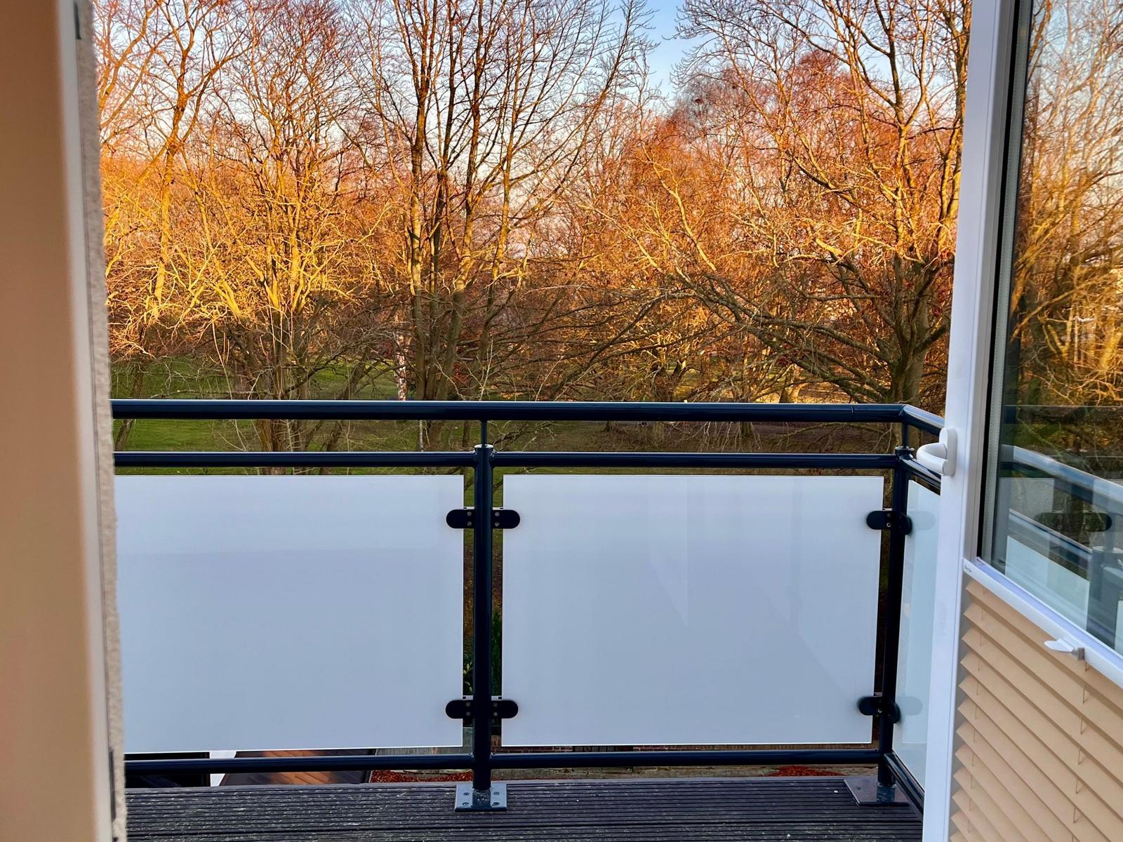Terrasse mit Glasgeländer und Blick auf einen Wald mit kahlen Bäumen.