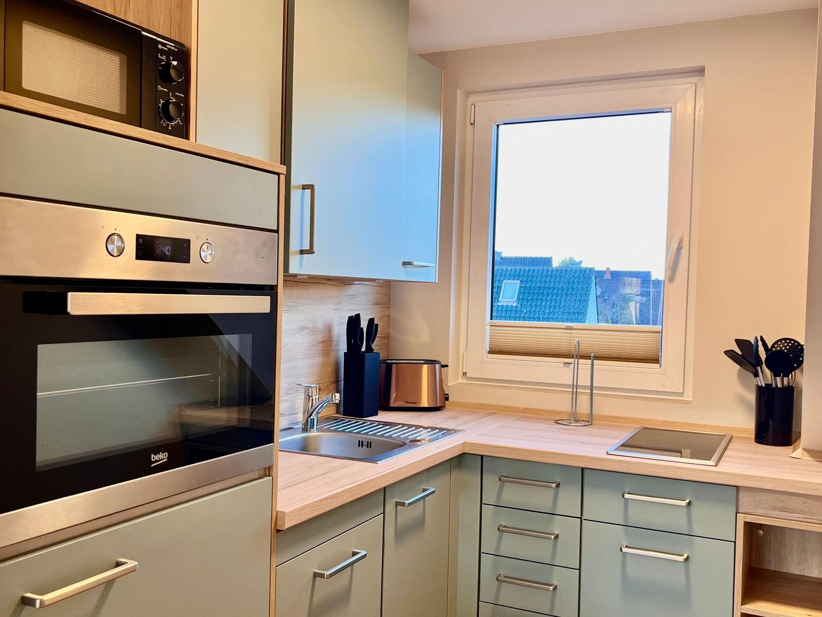 Küche mit Dunstabzug, Herd, Spüle und Fensterblick auf Dächer.