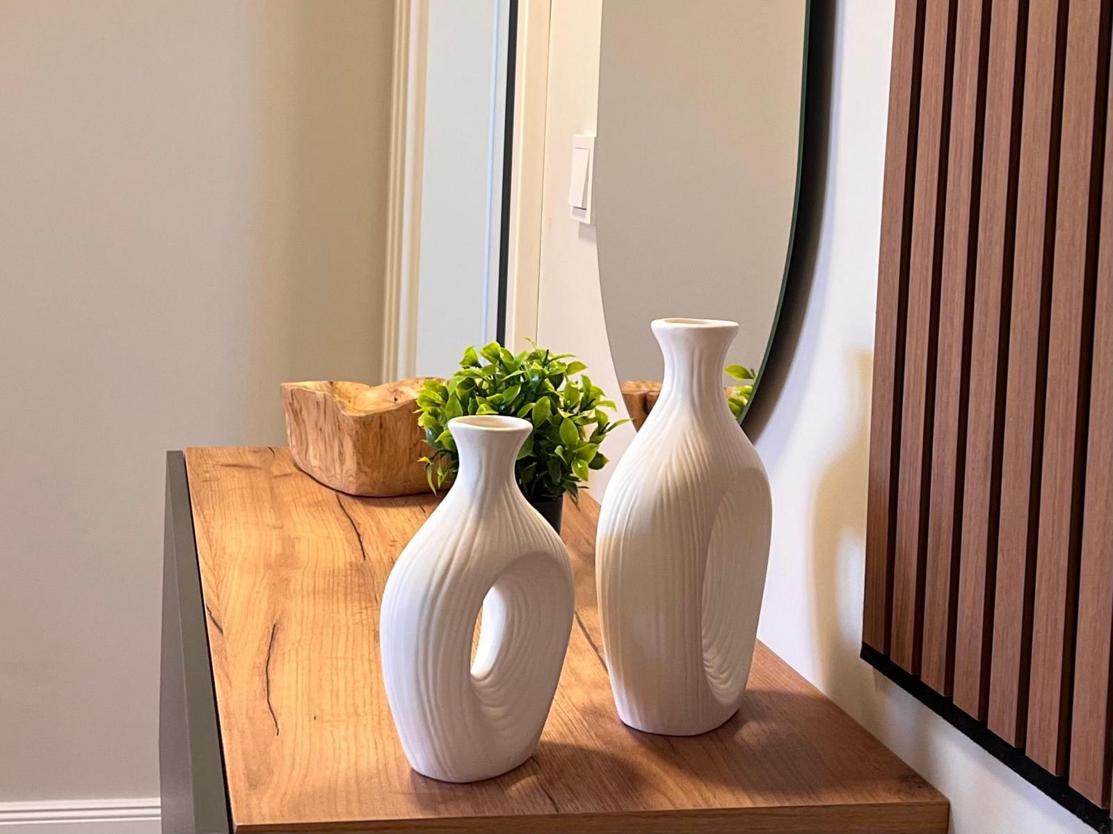 Holzkonsole mit zwei weißen Vasen, Pflanze und Holzschale. Spiegel und Holzpaneel an der Wand.