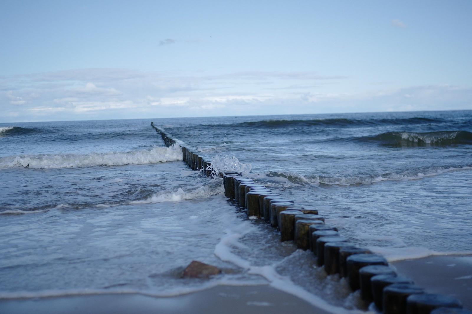Wellen brechen an einem Holzpfahlzaun am Strand.