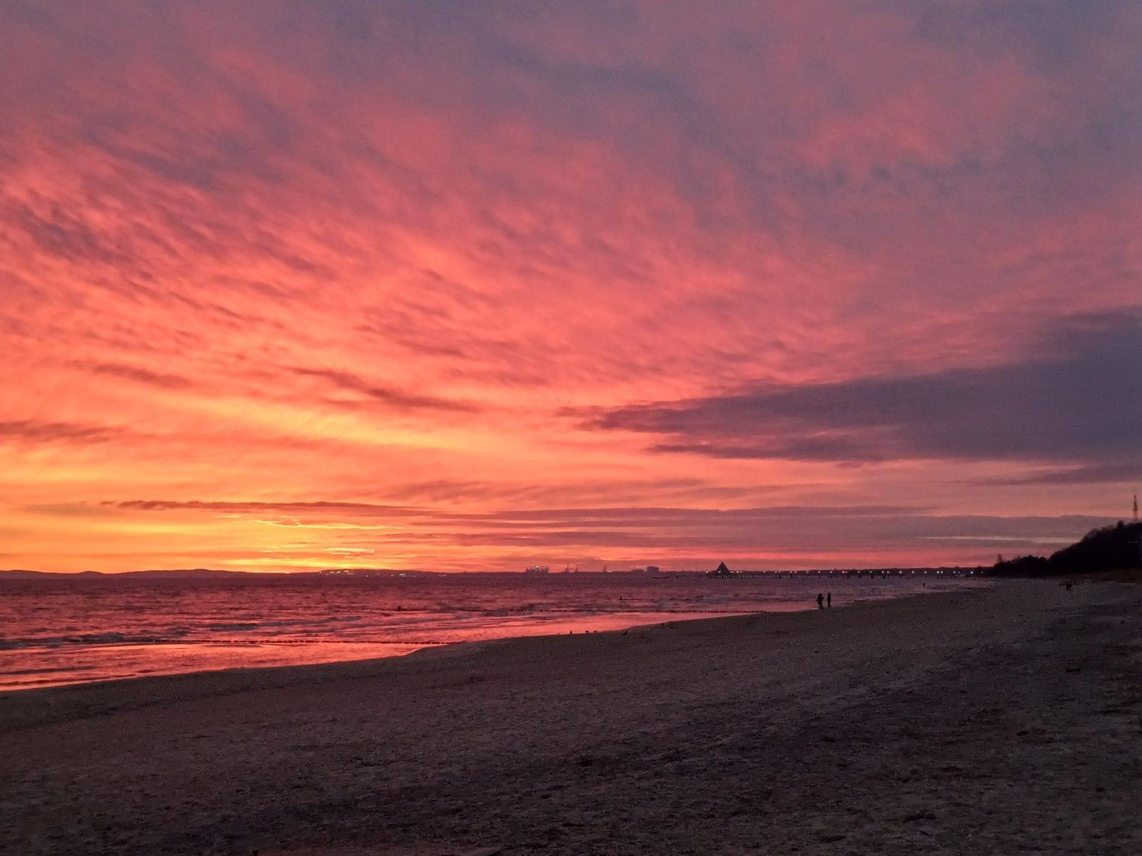 Sonnenuntergang über Strand mit leuchtendem Himmel und sanften Wellen.