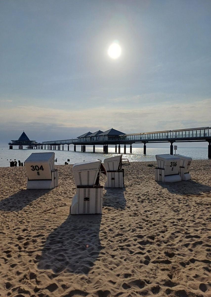 Strand mit Strandkörben und Steg im Hintergrund.