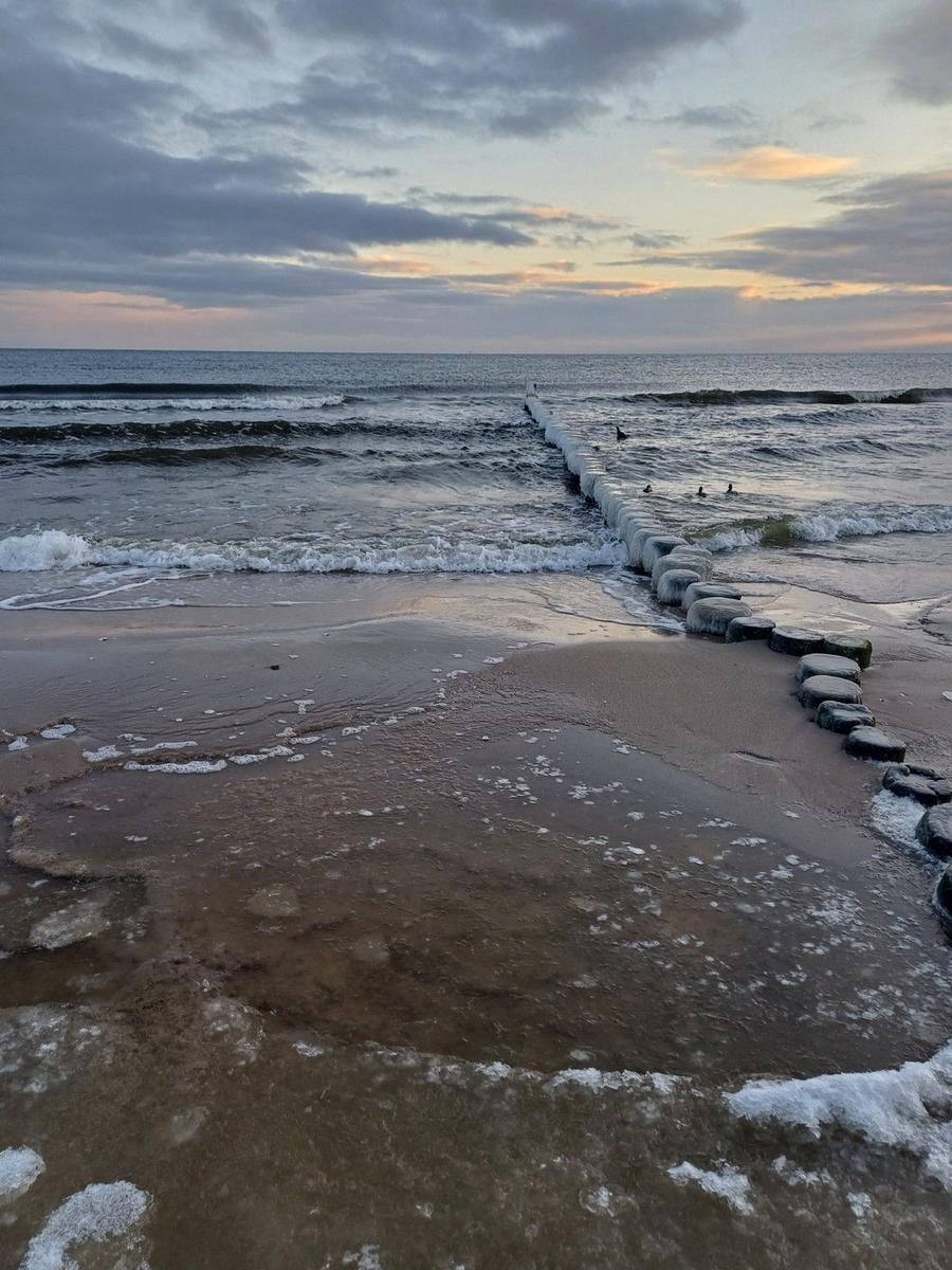 Strand mit Eis am Ufer und Steinen im Wasser bei Dämmerung.