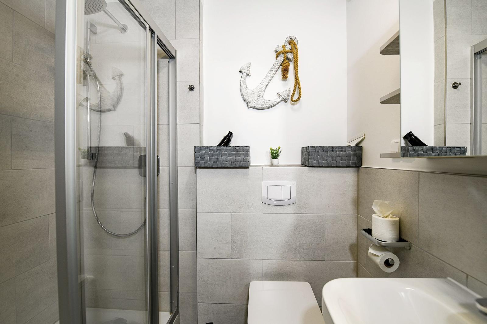 Badezimmer mit Dusche, Toilette und Waschbecken. Wanddekoration mit Anker.