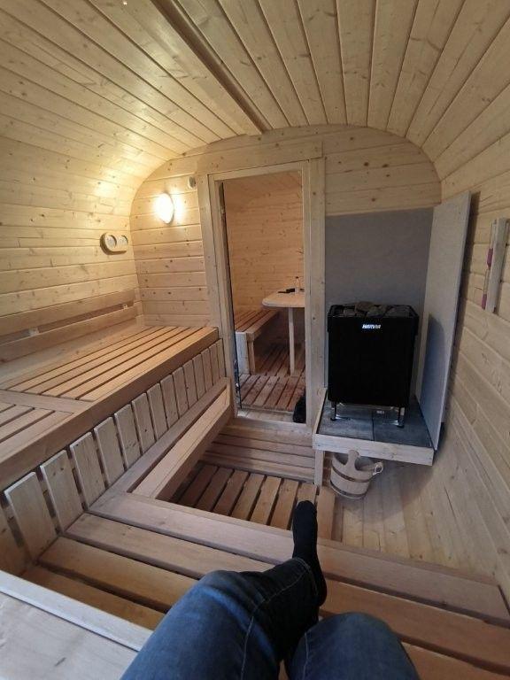 Sauna mit Holzbänken und Heizgerät. Durchgang zu einem weiteren Raum.