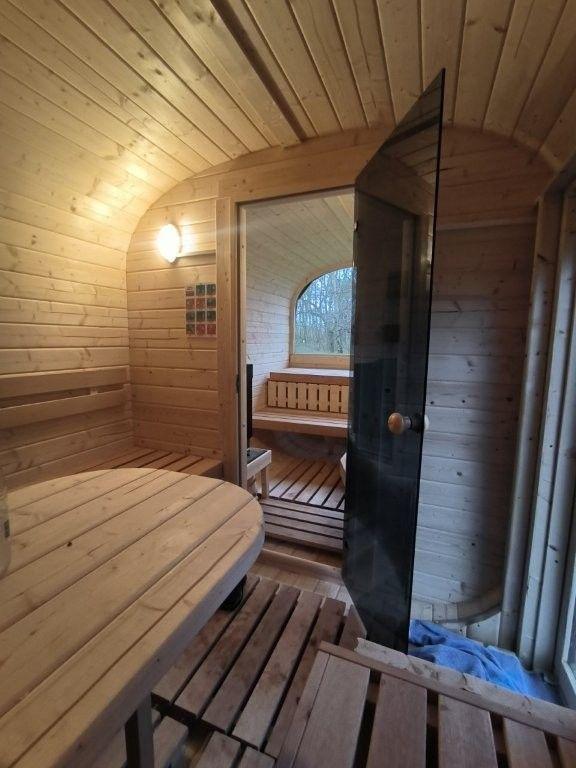Sauna mit Holzbank und runder Sitzfläche. Durchgang zu weiterem Raum mit Fenster.