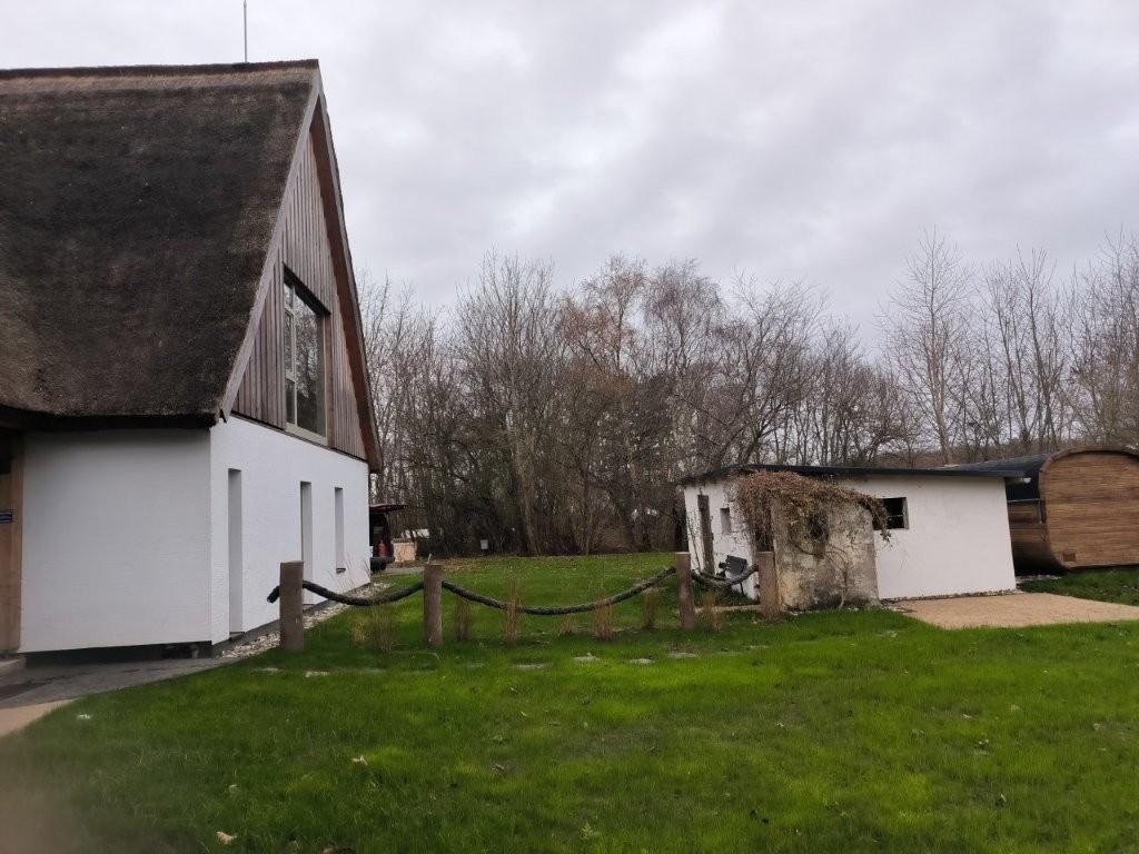 Haus mit Strohdach, grüner Rasen und kleiner Nebenstruktur im Hintergrund.