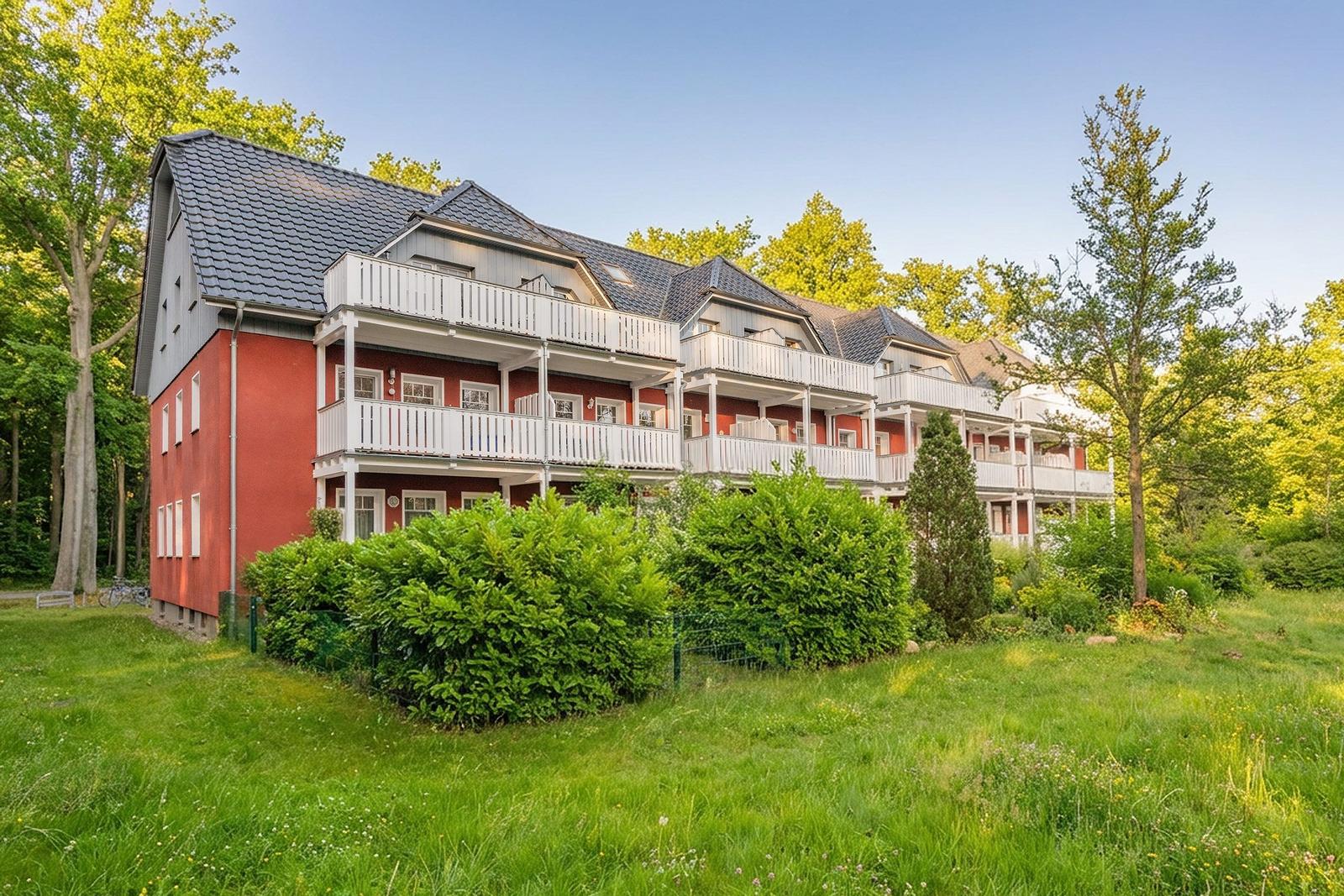 Rotes Mehrfamilienhaus mit weißen Balkonen und grüner Umgebung.