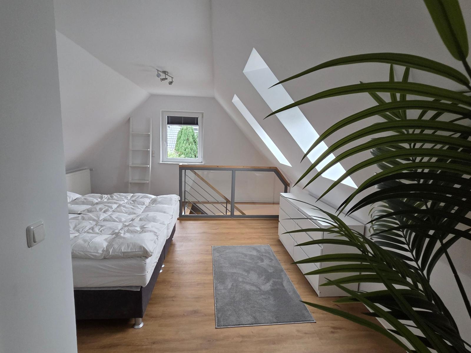 Schlafzimmer mit Dachschräge, Fenster, Bett, Schrank und Pflanze.