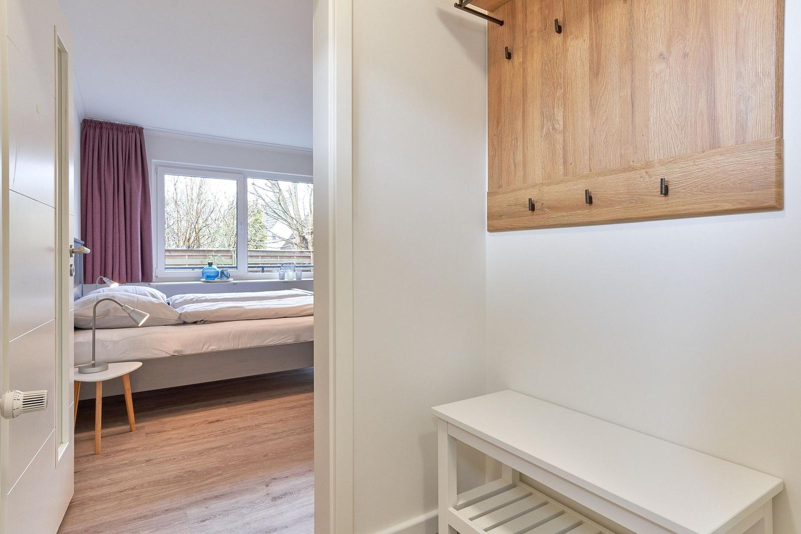 Schlafzimmer mit Bett, Fenster und Holzboden. Ankleidebereich mit Holzgarderobe und weißem Sitzbank.