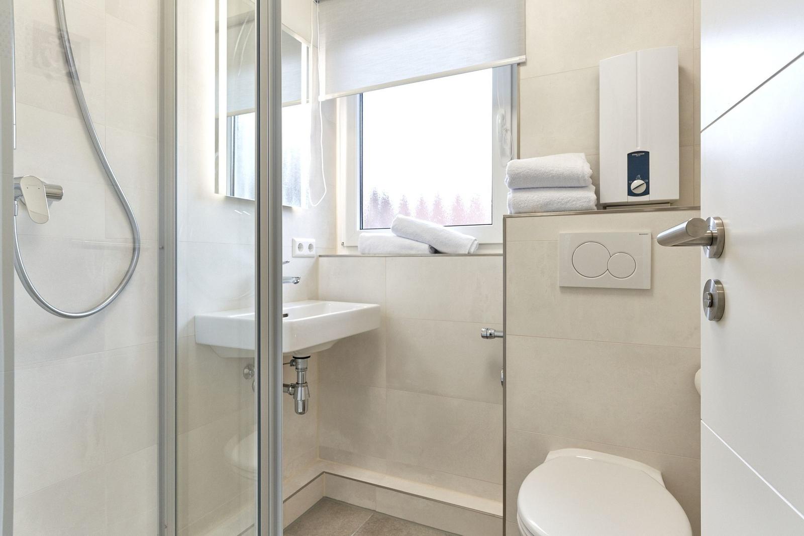 Badezimmer mit Dusche, Waschbecken und Toilette. Fenster mit Rollladen und Handtücher.