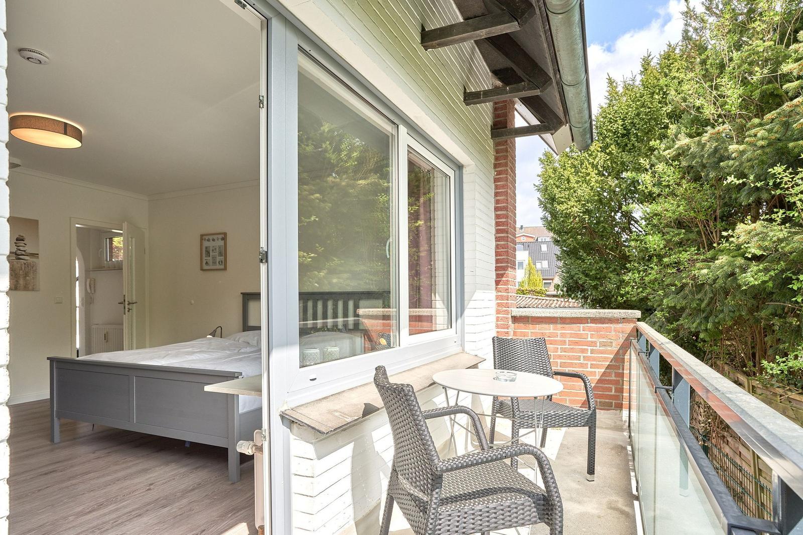 Schlafzimmer mit Balkon, Tisch und Stühlen. Blick auf grüne Bäume.