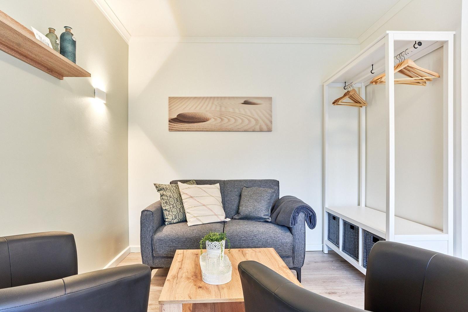Ein Wohnzimmer mit grauem Sofa, Holztisch und Kleiderschrank mit Haken.