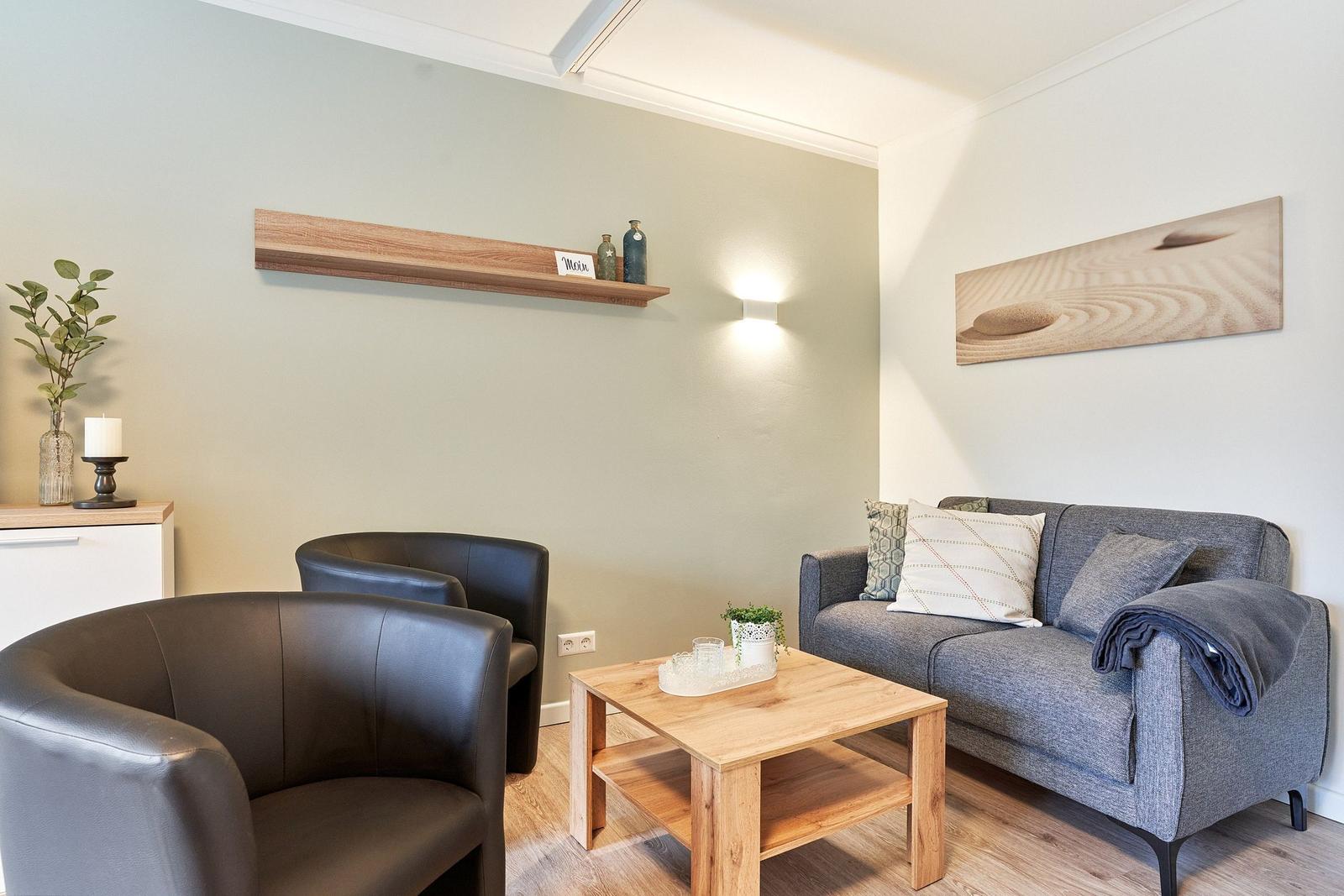 Ein Wohnzimmer mit grauem Sofa, zwei schwarzen Sesseln und einem Holztisch.