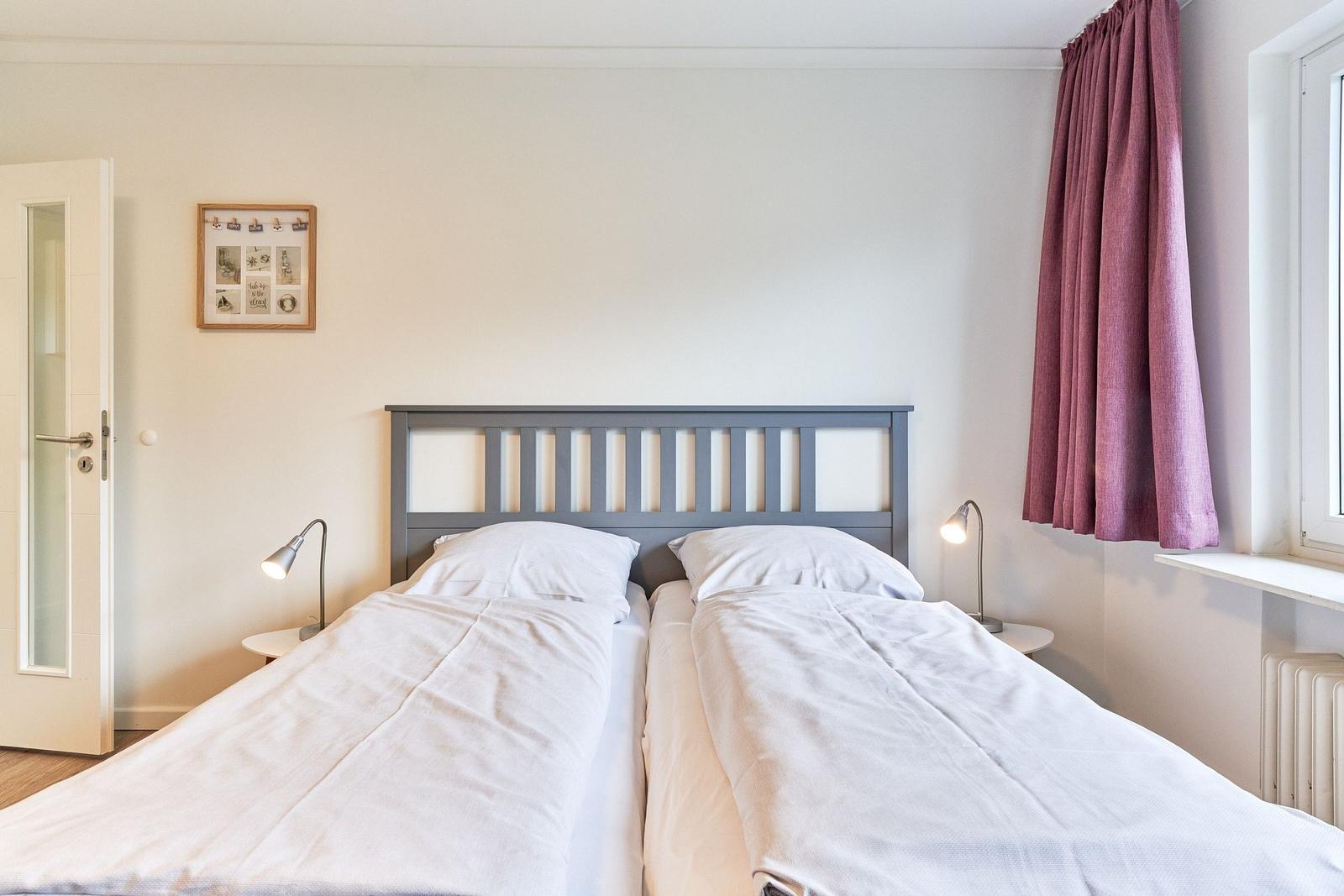 Zwei Betten mit weißen Bettwäsche, Nachttische und Lampen, Fenster mit lila Vorhang.