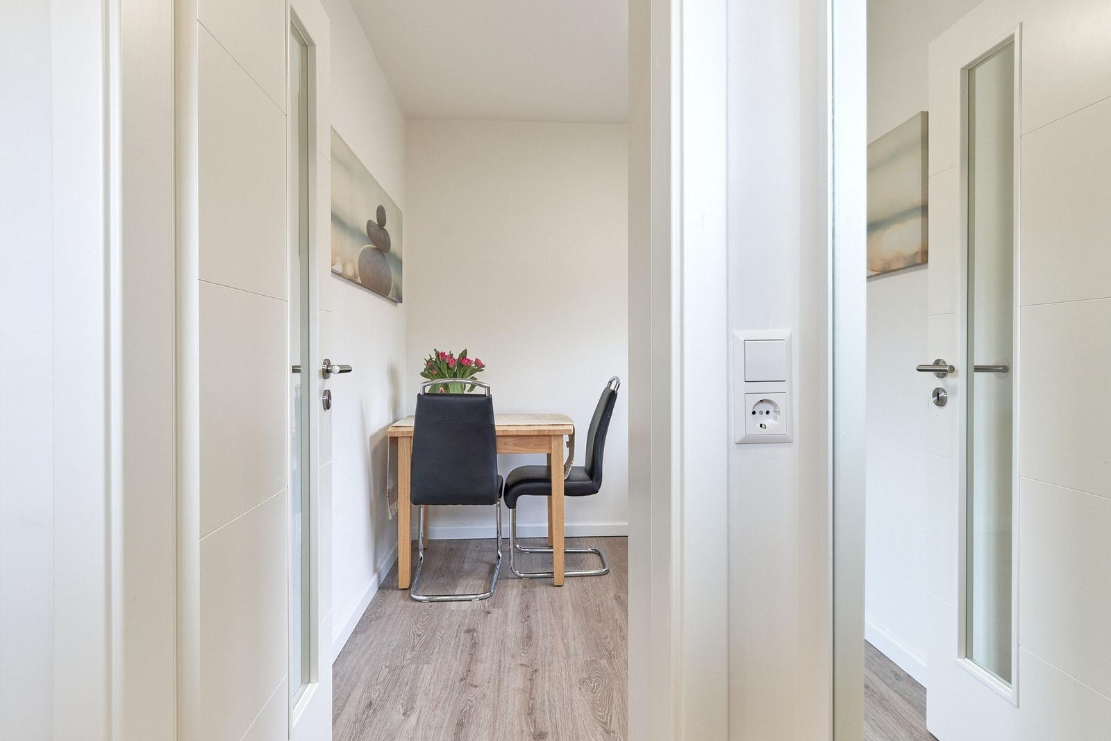 Essbereich mit Tisch, zwei Stühlen und Blumen. Wandbild und Holzboden.