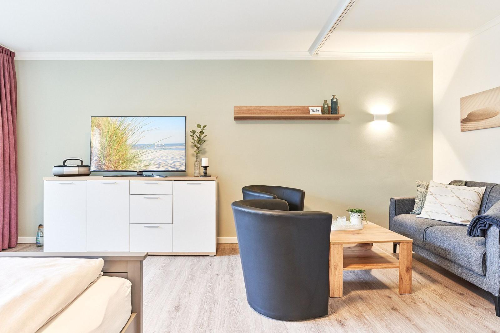 Wohnzimmer mit Sofa, zwei Sesseln, Couchtisch und Fernseher auf Schrank.