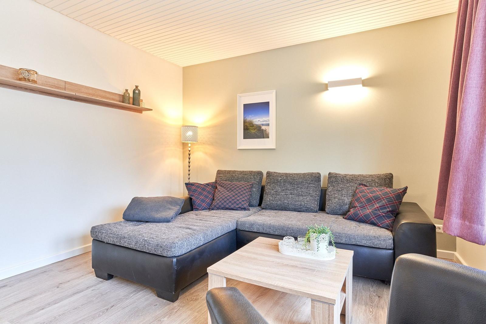 Ein Wohnzimmer mit einem grauen Sofa, einem Holztisch und einer Wandlampe.