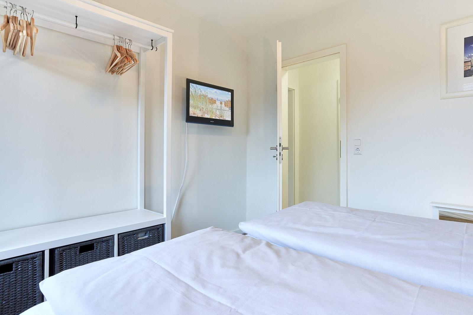 Zwei Betten, Kleiderschrank mit Haken und Wandfernseher in einem Schlafzimmer.