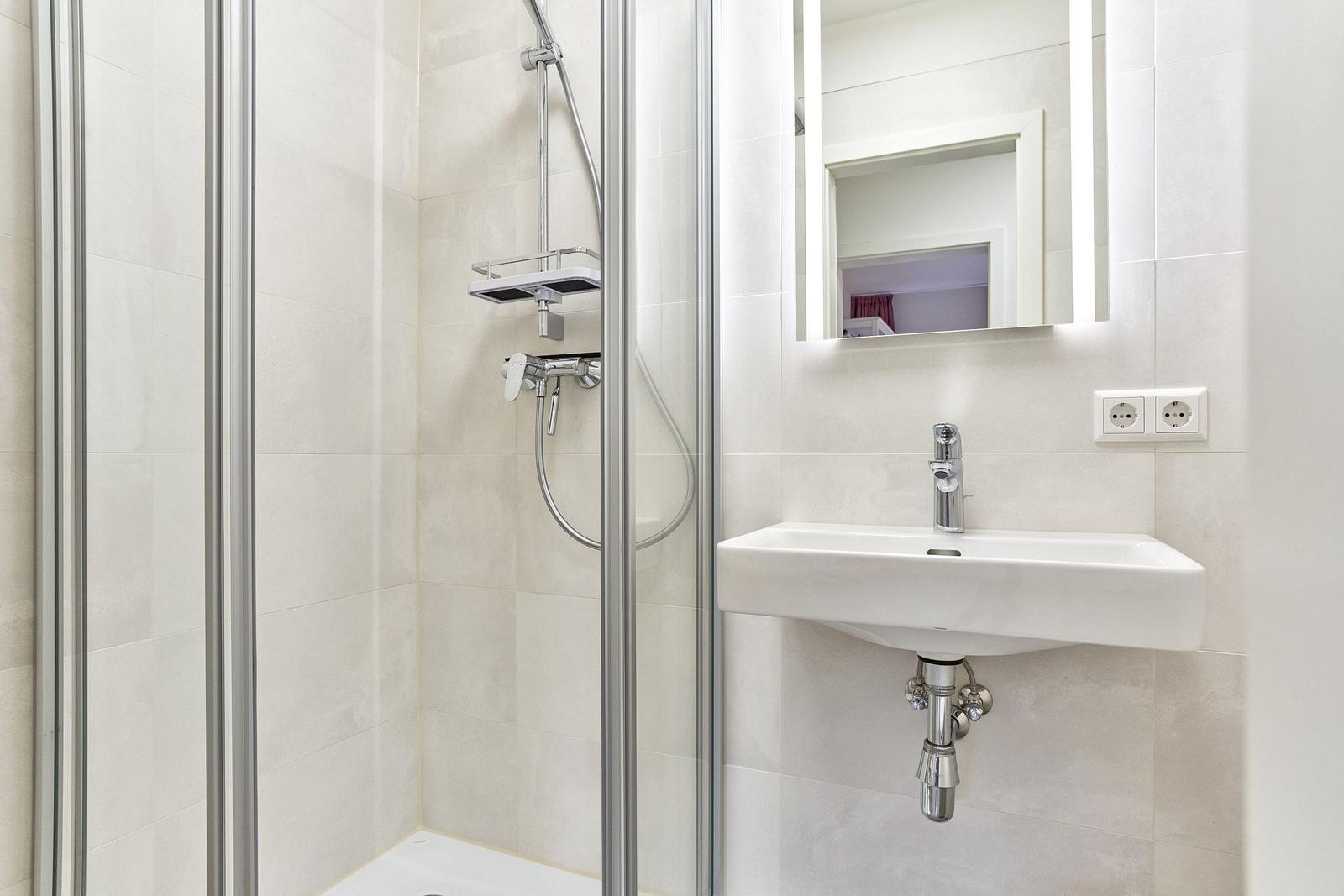 Dusche mit Duschbrause und Waschbecken mit Spiegel