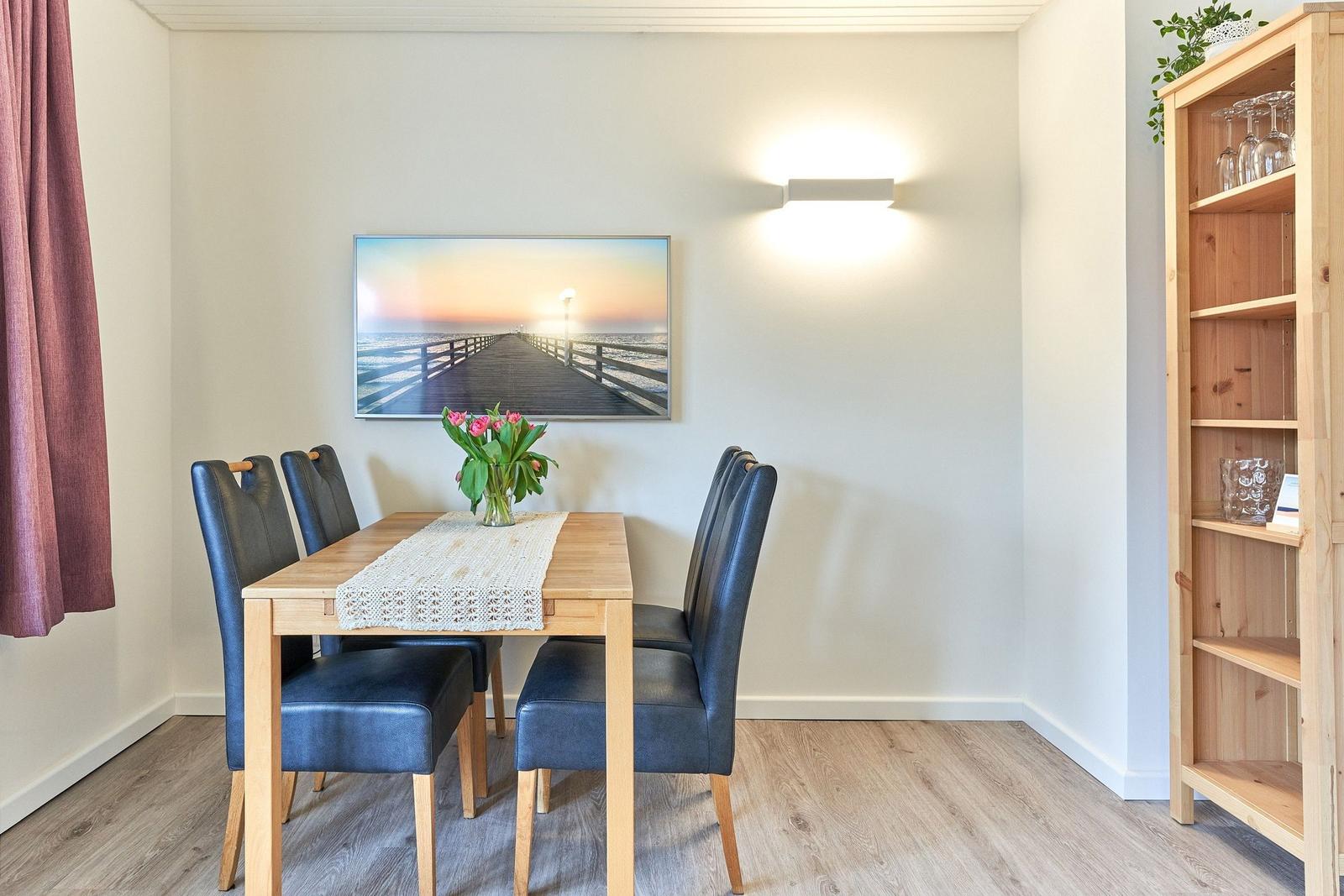 Esszimmer mit Holztisch, vier Stühlen, Wandbild und Bücherregal.