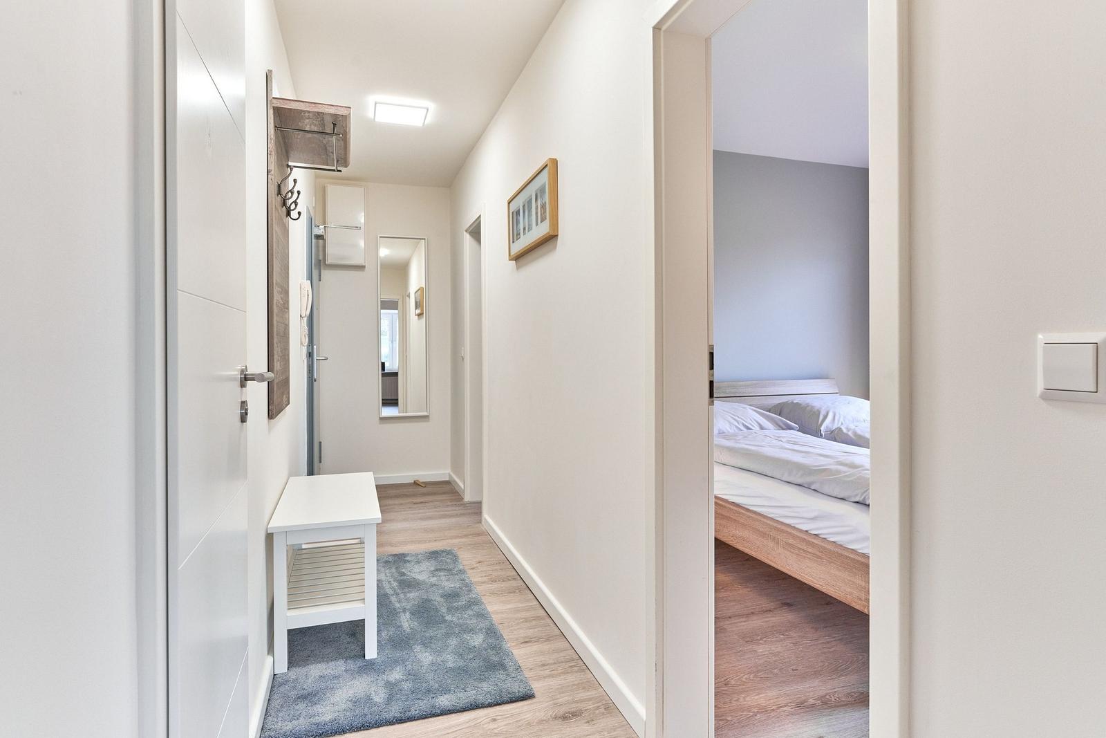 Flur mit Kleiderhaken und Tisch. Im Hintergrund Schlafzimmer mit Bett.
